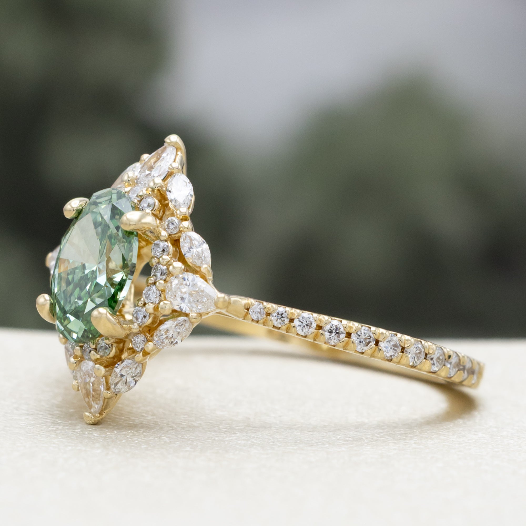 Gold ring with a green lab diamond and diamond accents on a neutral background