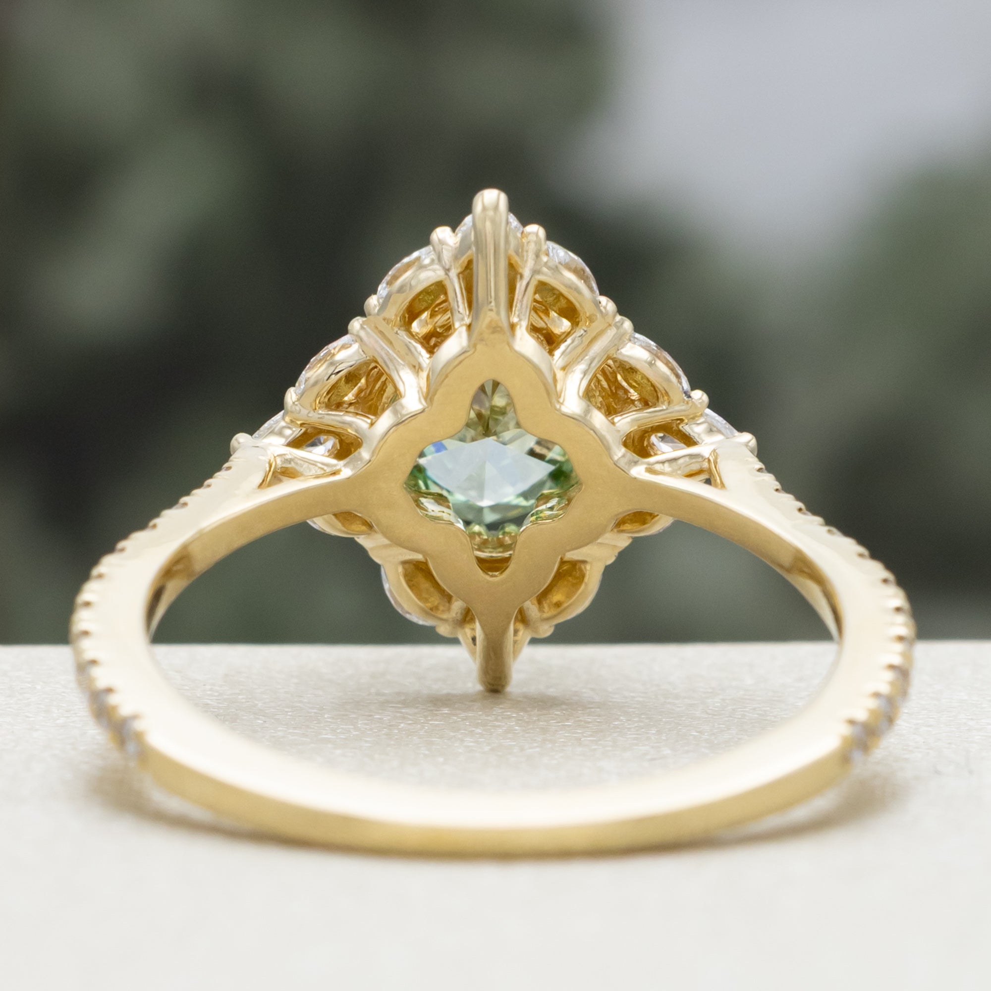 Gold ring with a green lab diamond and diamond accents on a neutral background