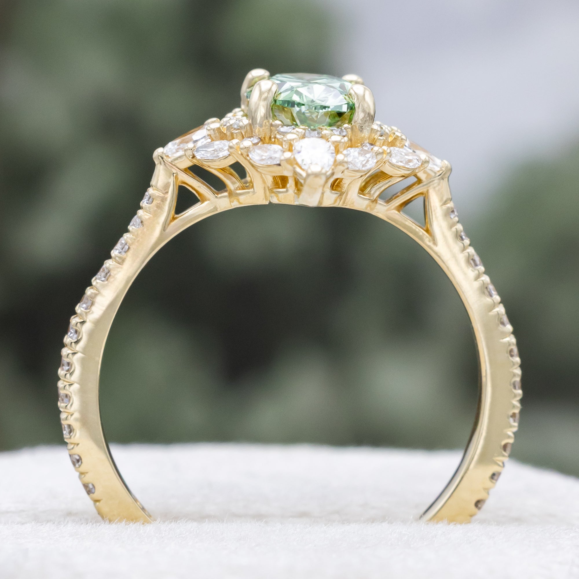 Gold ring with a green lab diamond and diamond accents on a neutral background