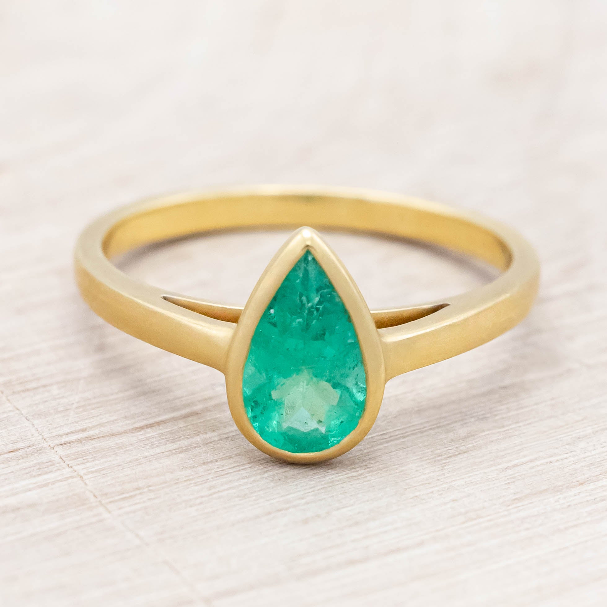 Gold ring with a pear cut emerald on a light wooden background