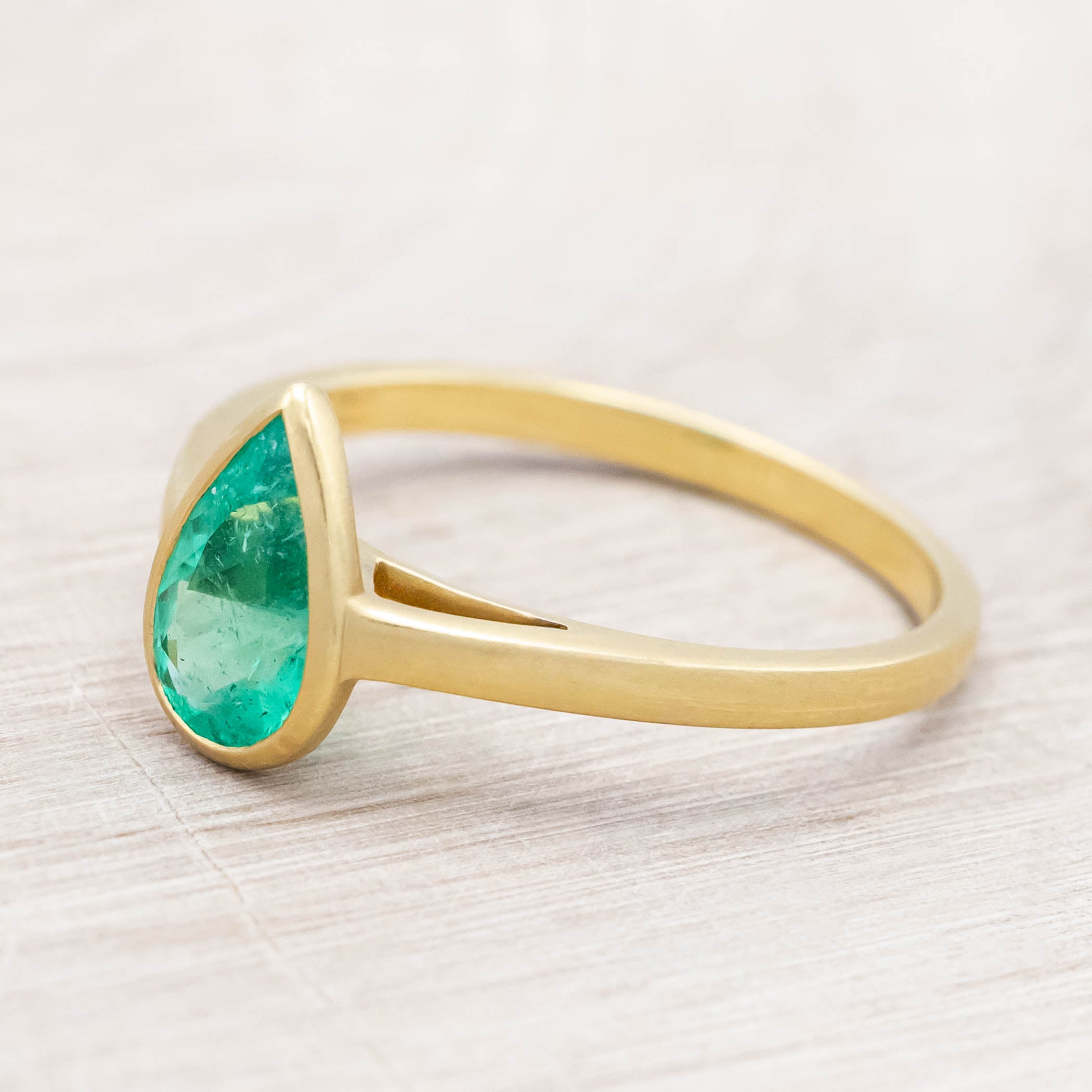 Gold ring with a pear cut emerald on a light wooden background