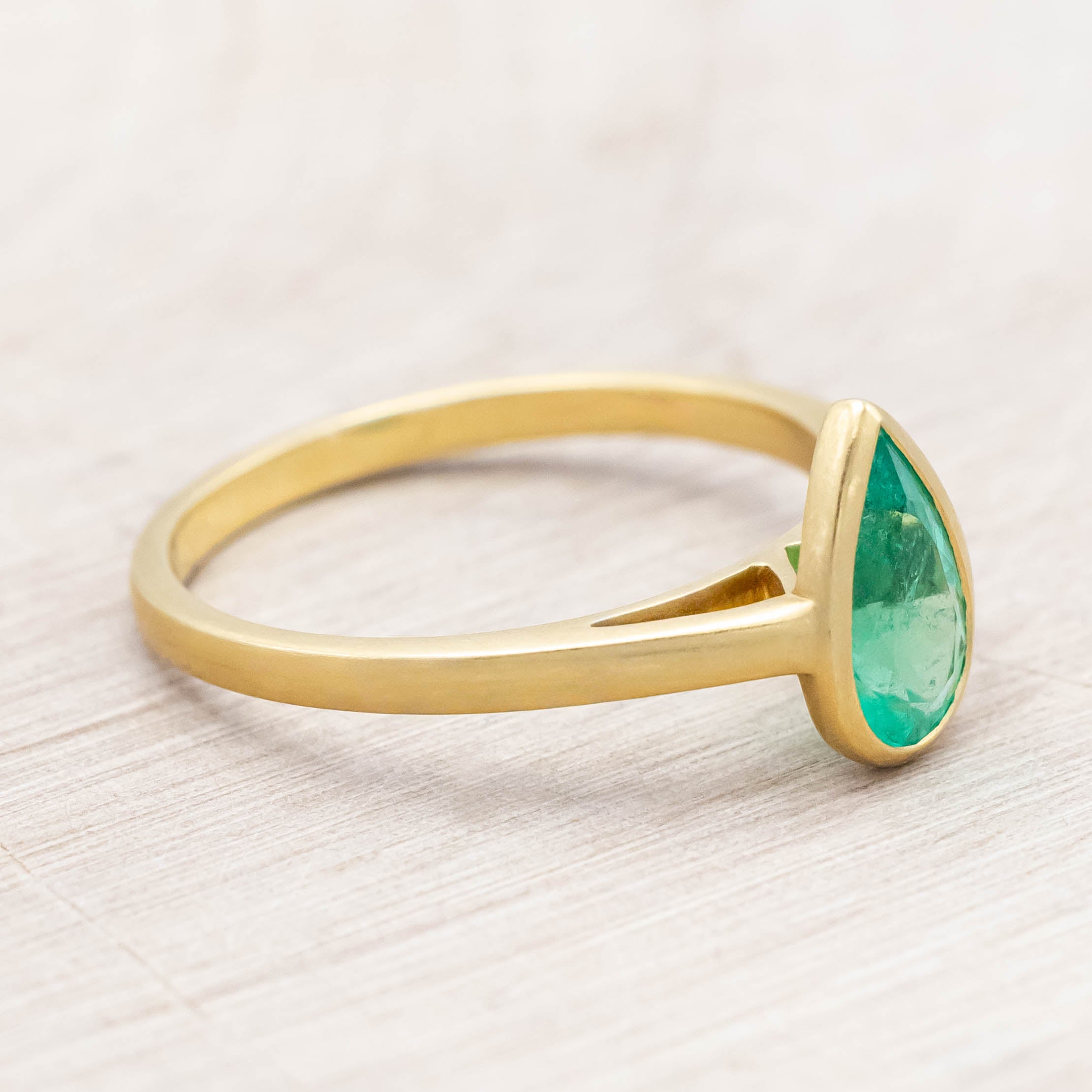 Gold ring with a pear cut emerald on a light wooden background