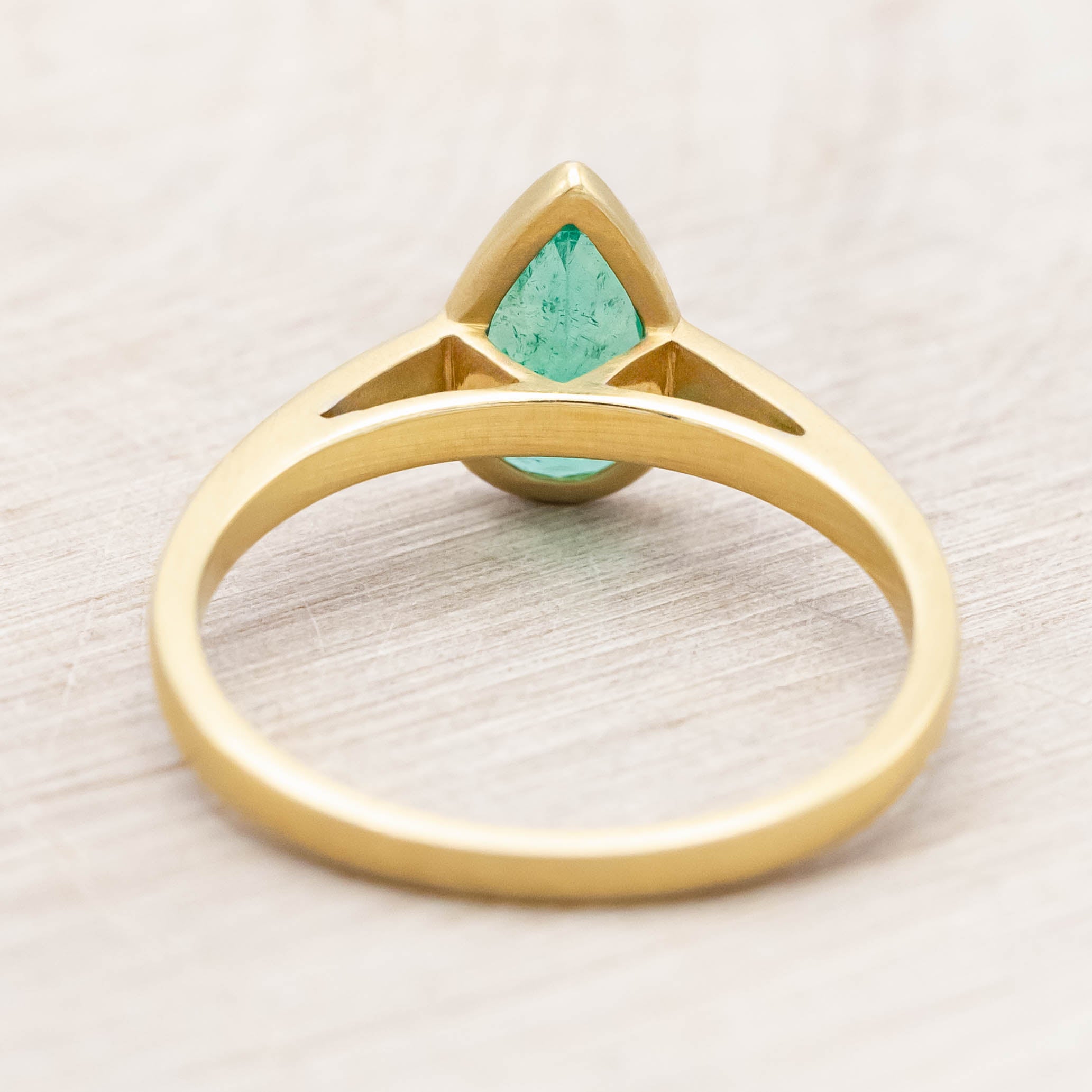 Gold ring with a pear cut emerald on a light wooden background