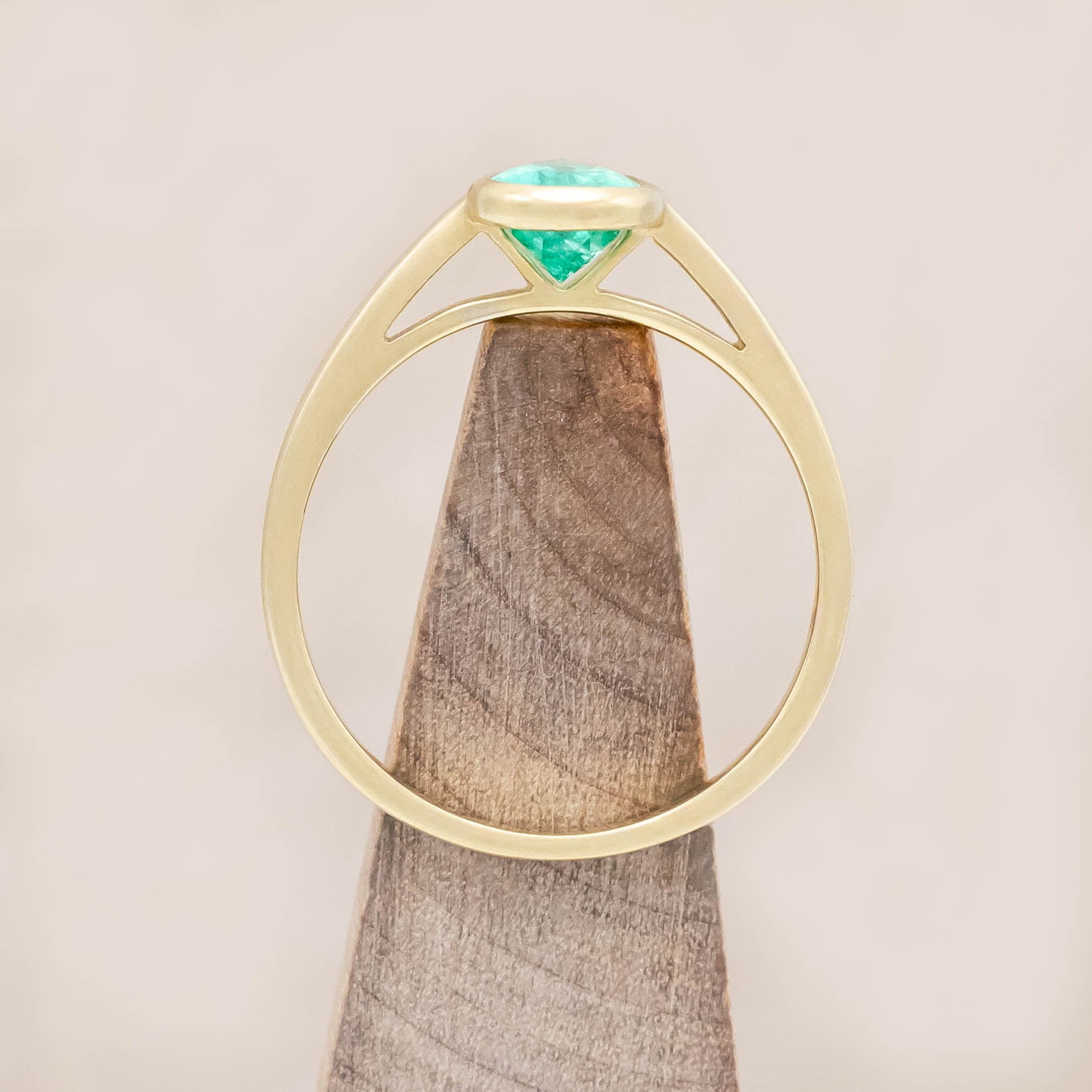 Gold ring with a pear cut emerald on a wooden stand against a beige background