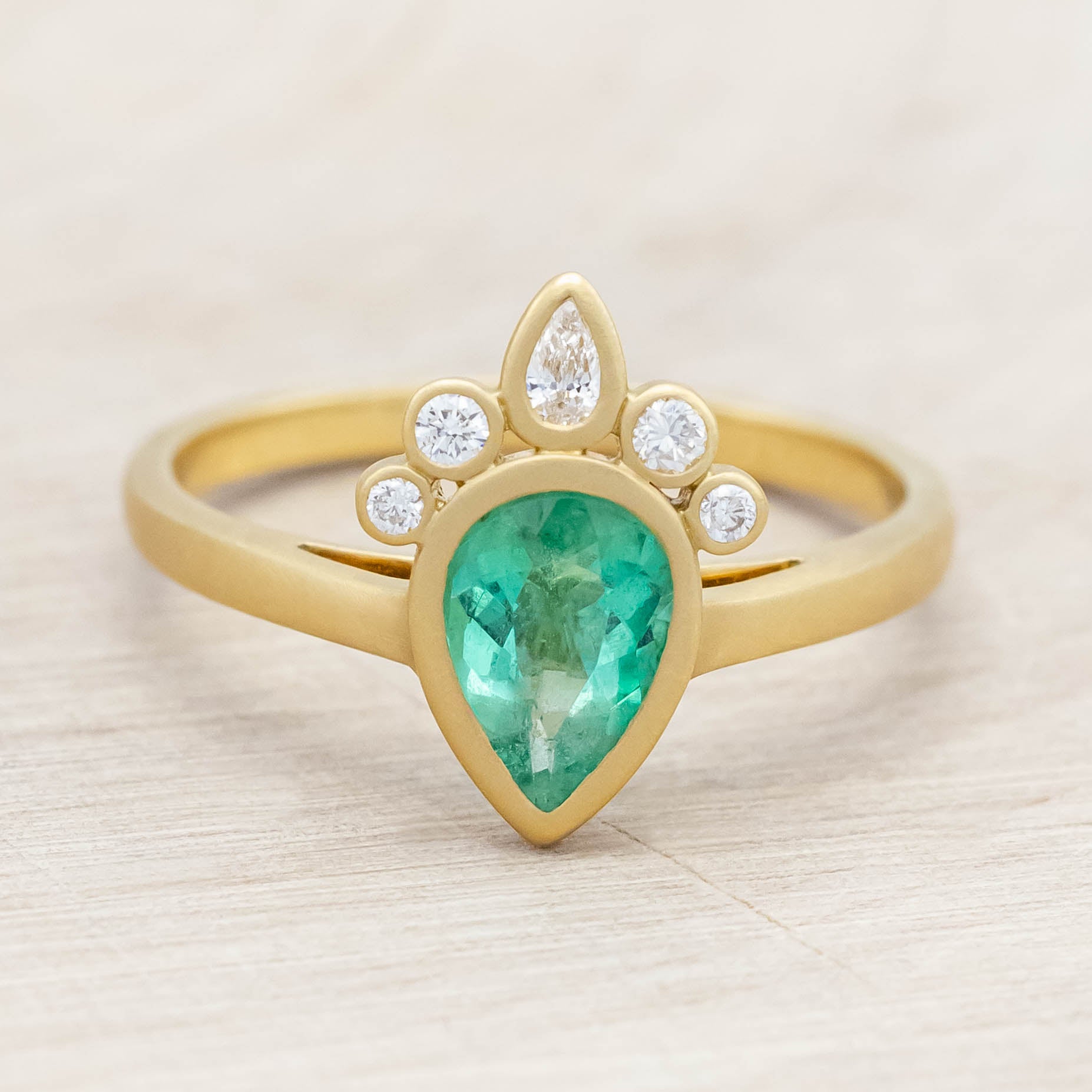 Gold ring with a green emerald and small diamonds on light wooden background