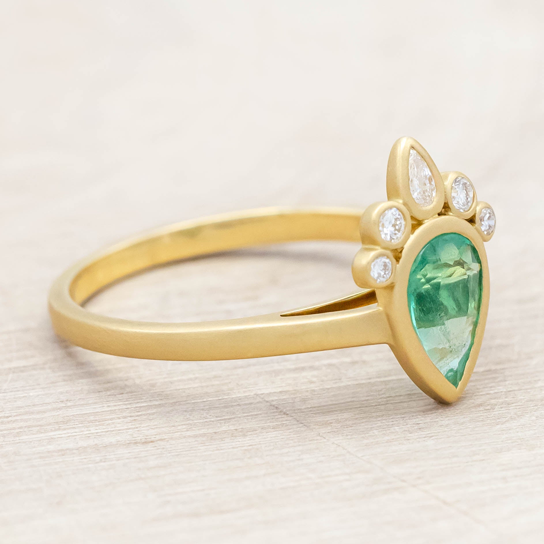 Gold ring with a green emerald and small diamonds on light wooden background