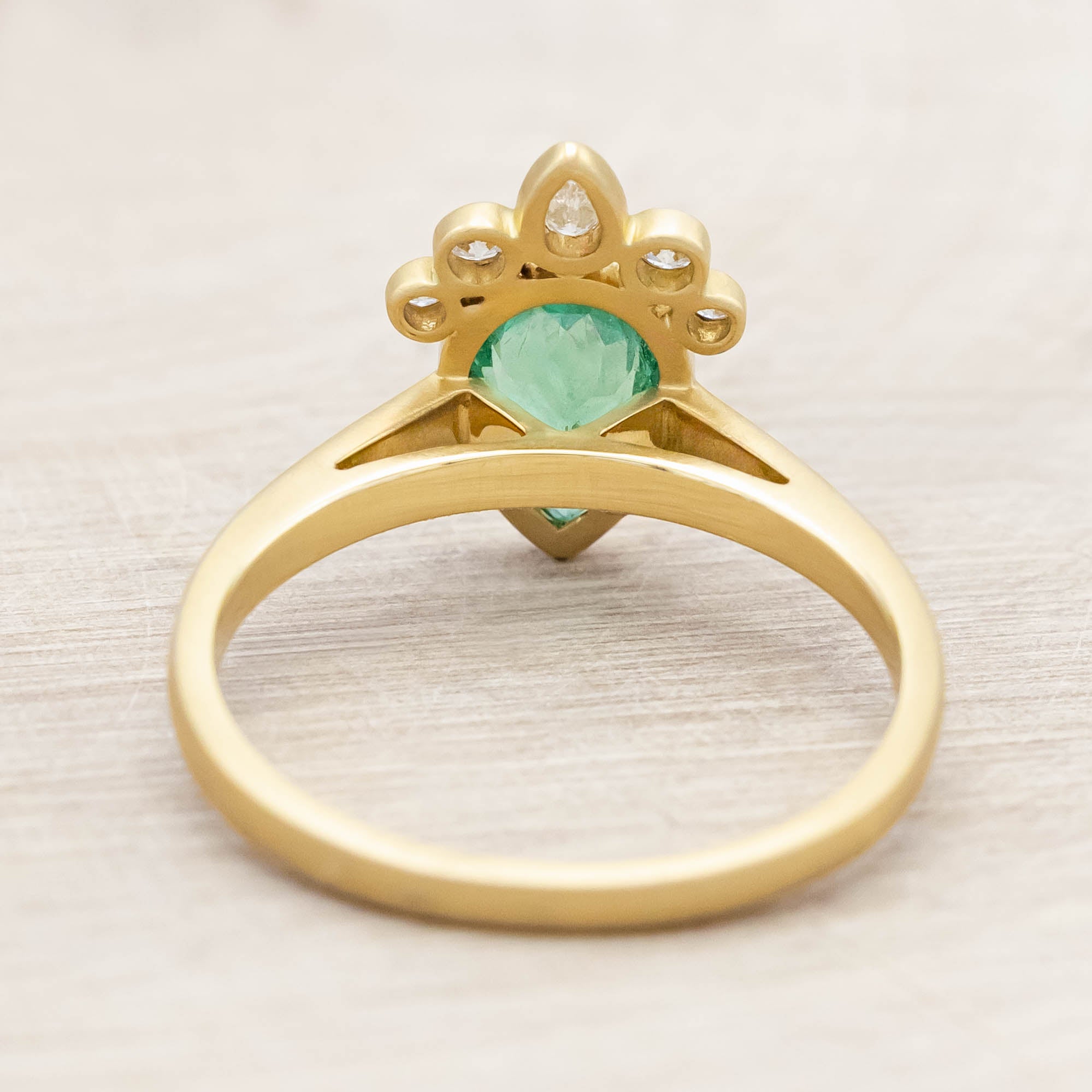 Gold ring with a green emerald and small diamonds on light wooden background