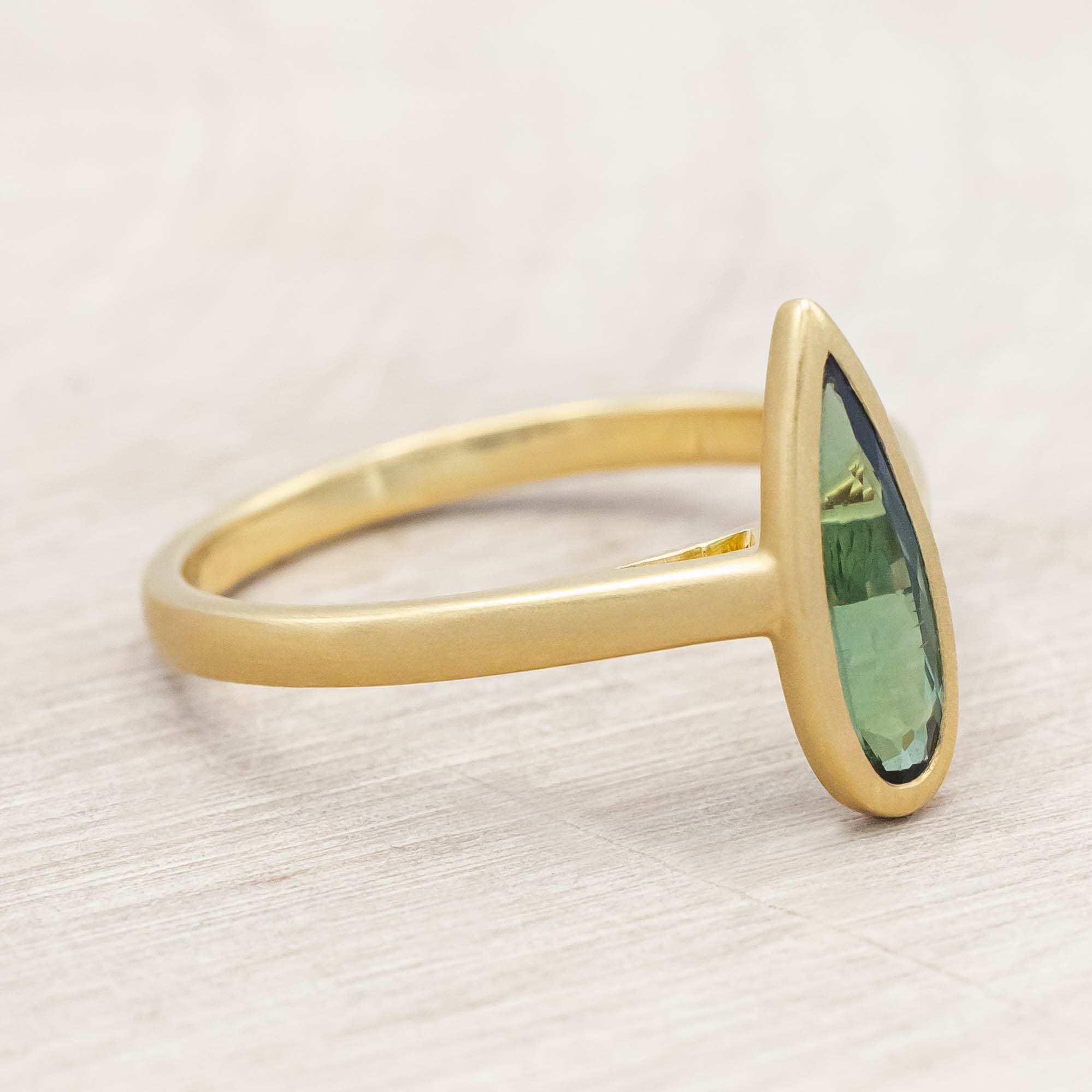 Gold ring with a green tourmaline gemstone on a light wooden surface