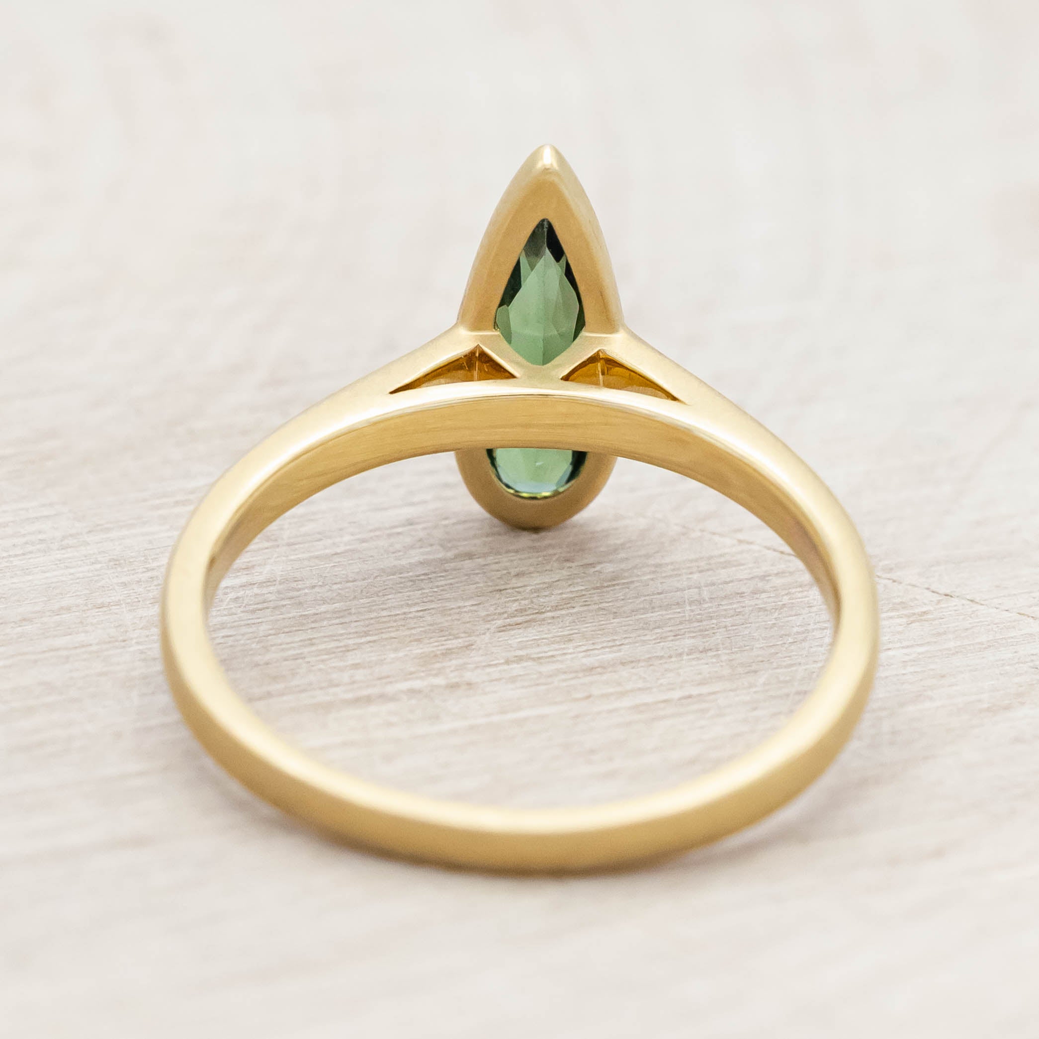 Gold ring with a green tourmaline gemstone on a light wooden surface