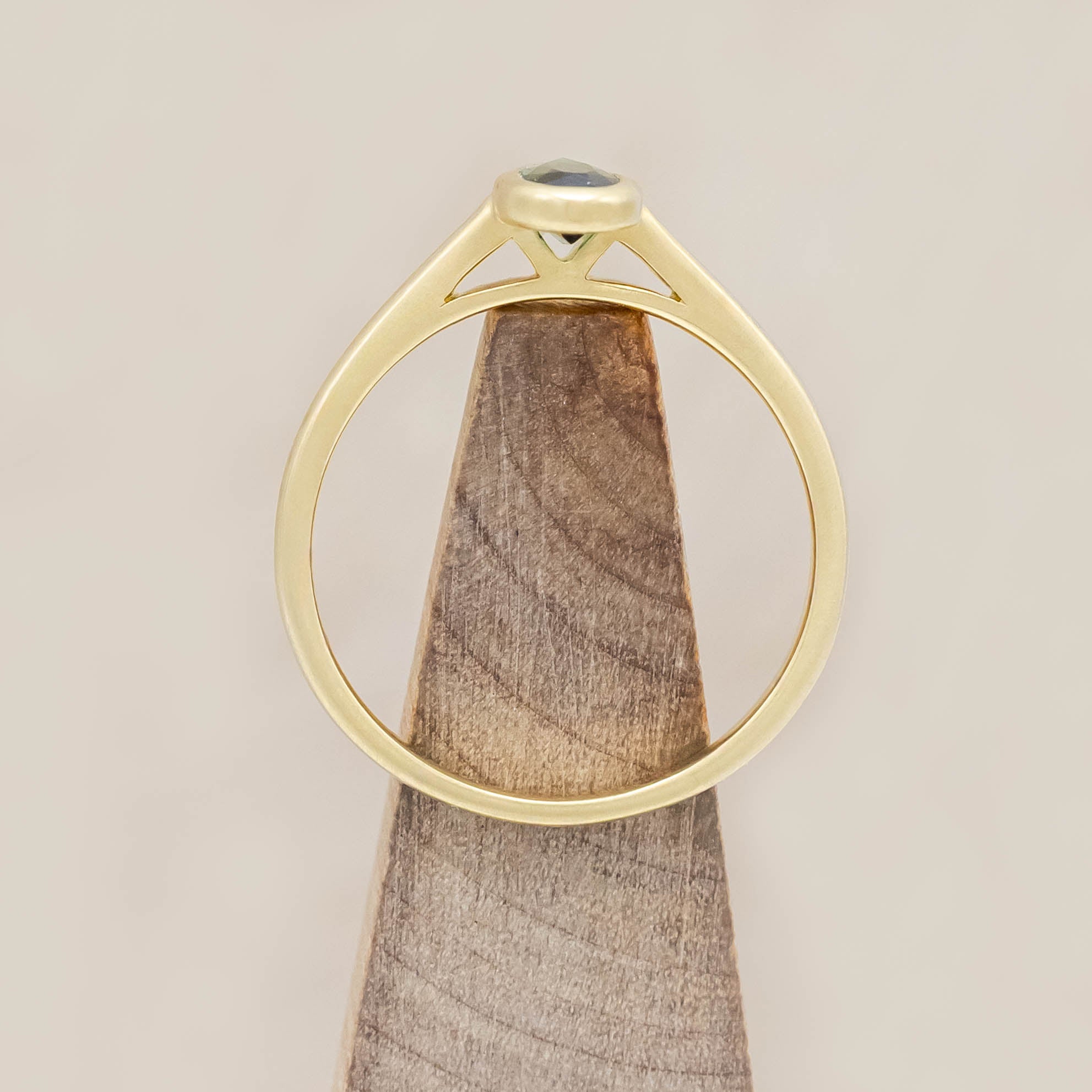 Gold ring with a green tourmaline gemstone on a wooden block against a beige background