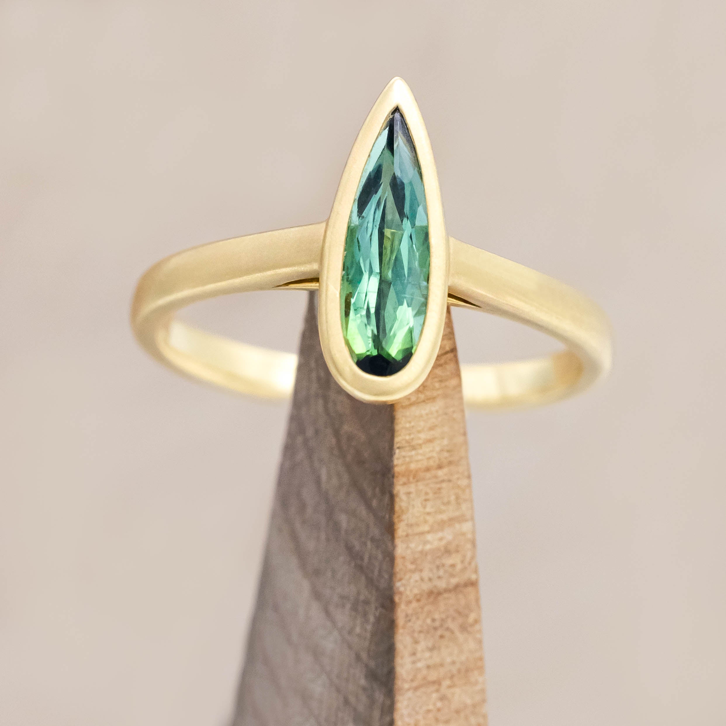 Gold ring with a green tourmaline gemstone on a wooden stand against a beige background