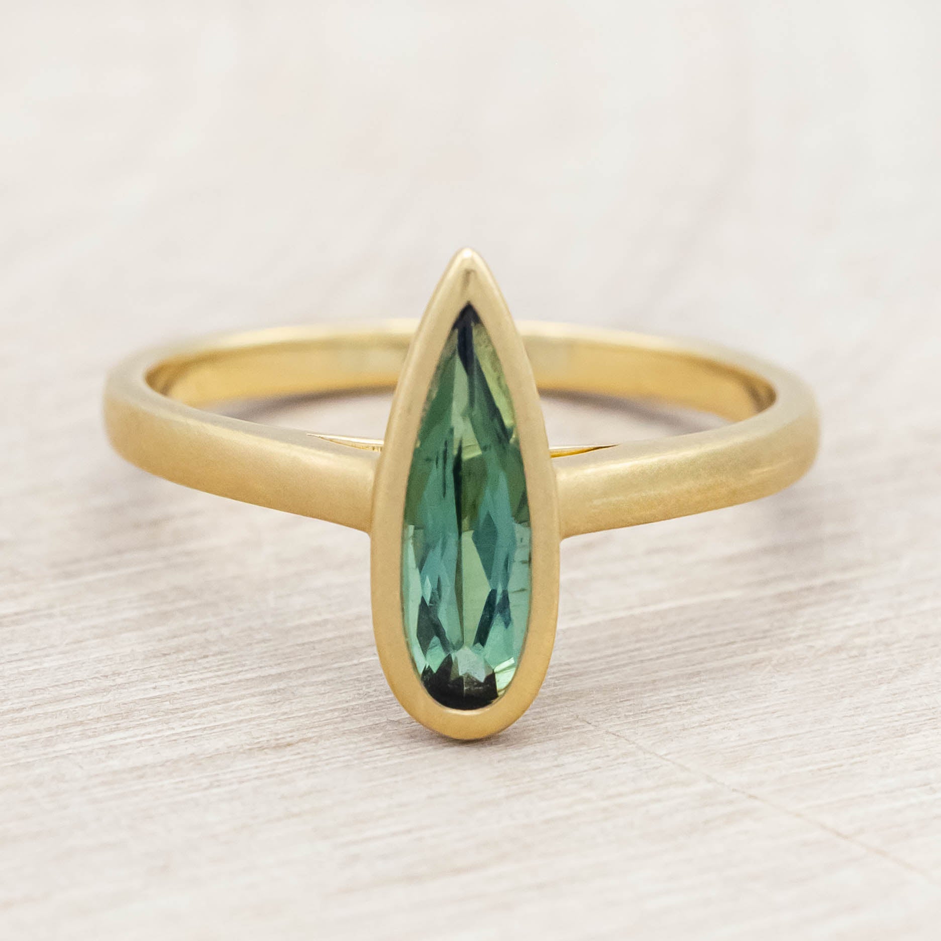 Gold ring with a green tourmaline gemstone on a light wooden surface