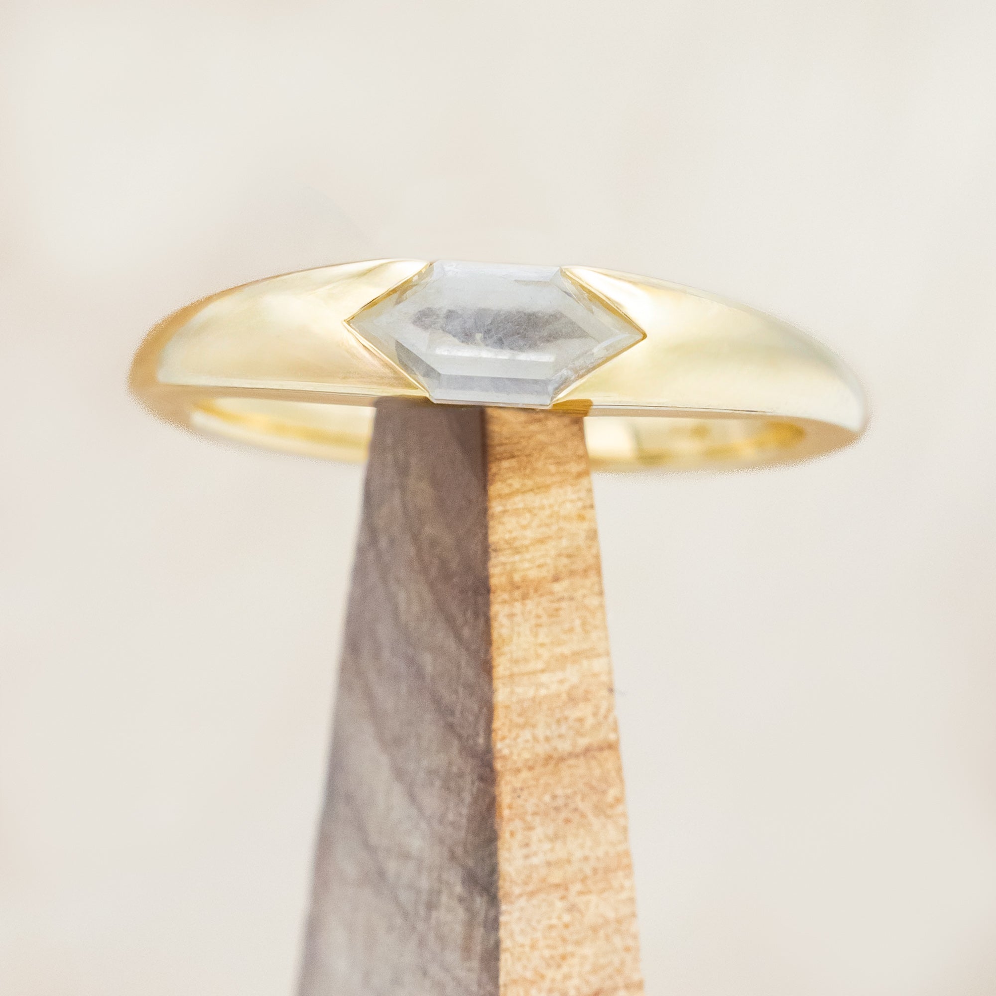 14K gold ring with a geometric stone on a wooden stand against a light background