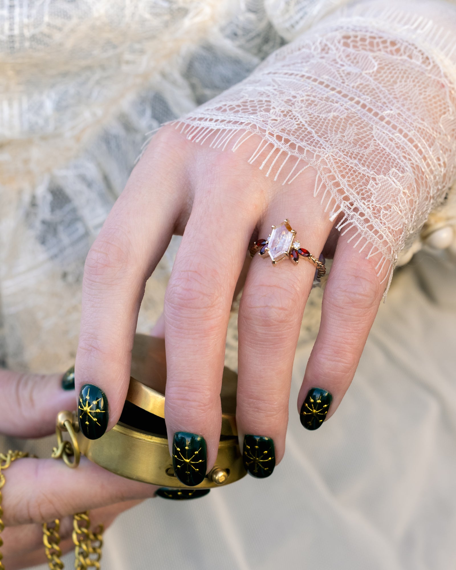 Hand wearing gold ring with lace sleeve holding a metal box