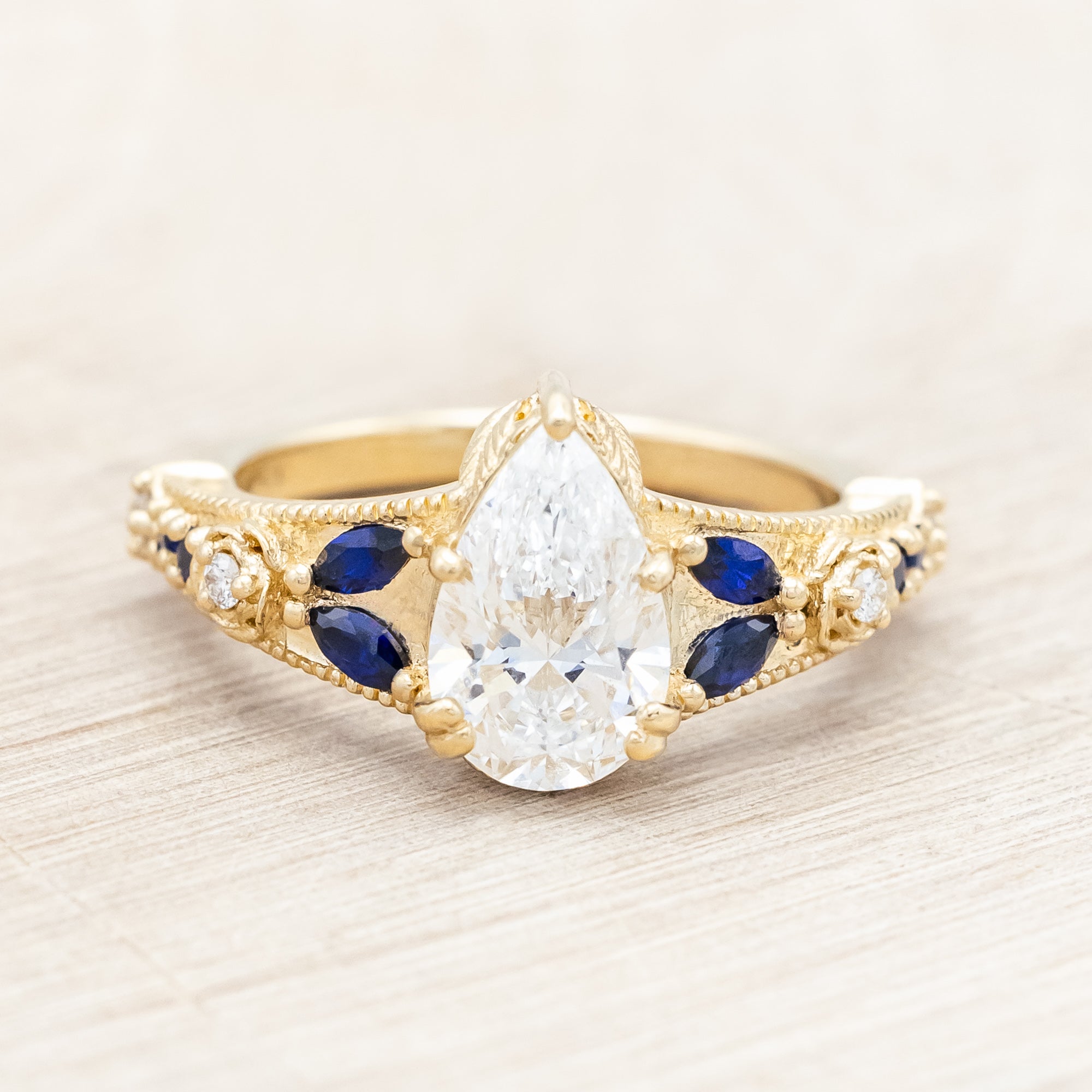 14K yellow gold ring with lab diamond and blue sapphires on a beige background