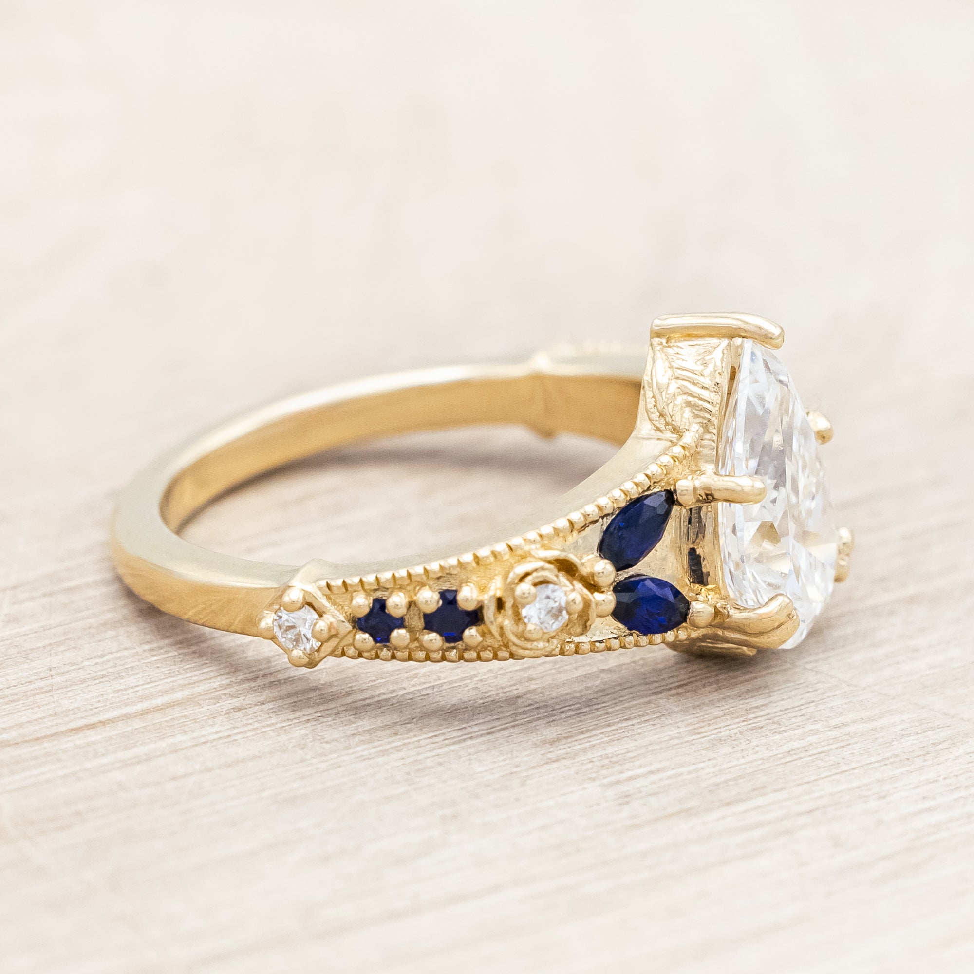 14K yellow gold ring with lab diamond and blue sapphires on a beige background
