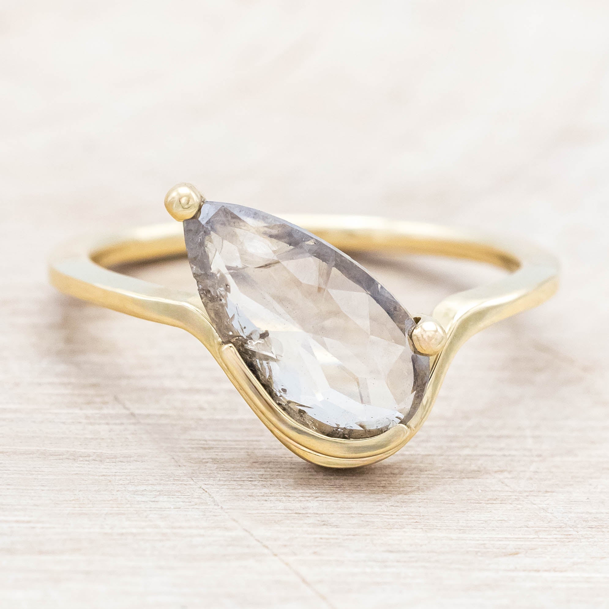 Gold ring with a salt & pepper diamond on a light wooden background