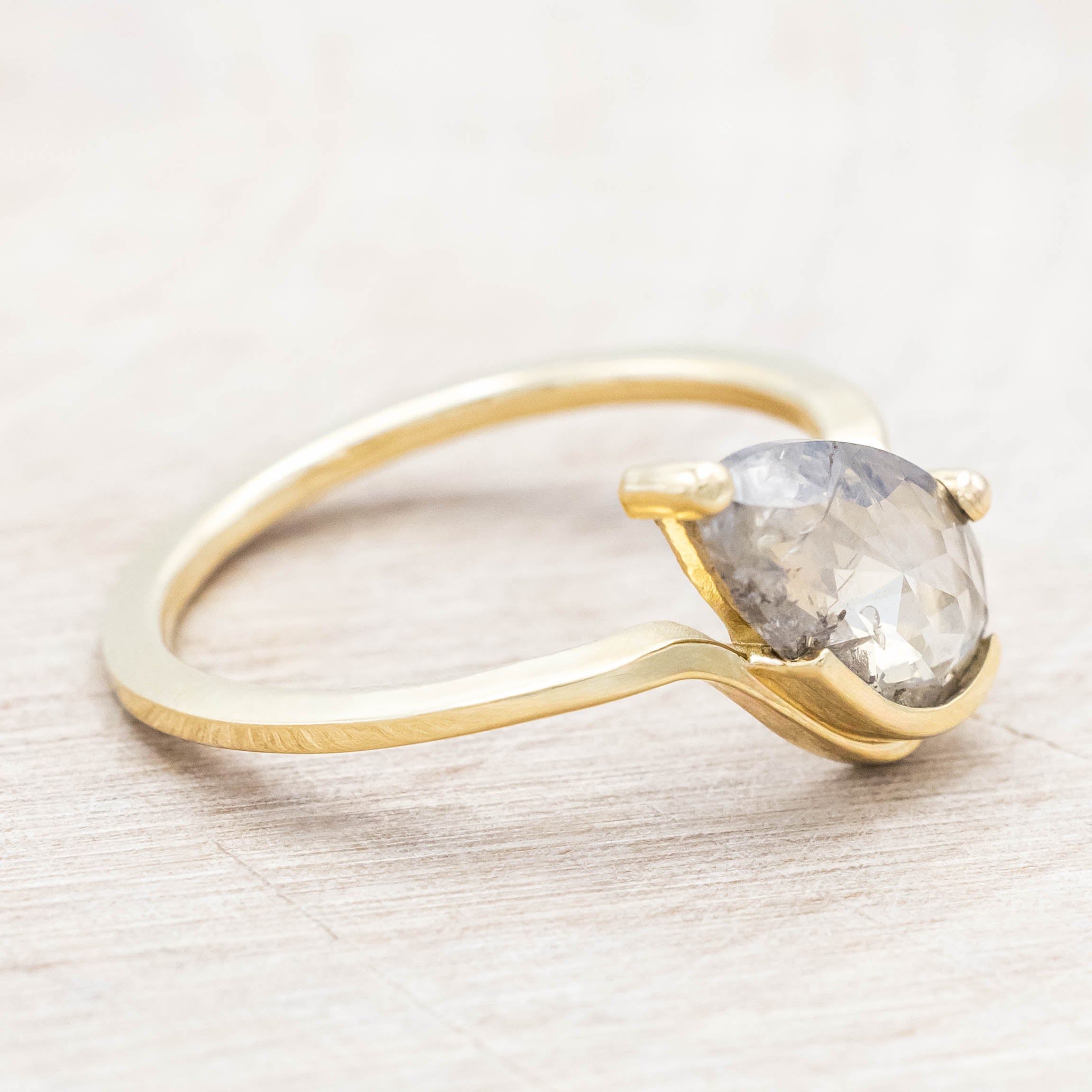 Gold ring with a salt & pepper diamond on a light wooden background