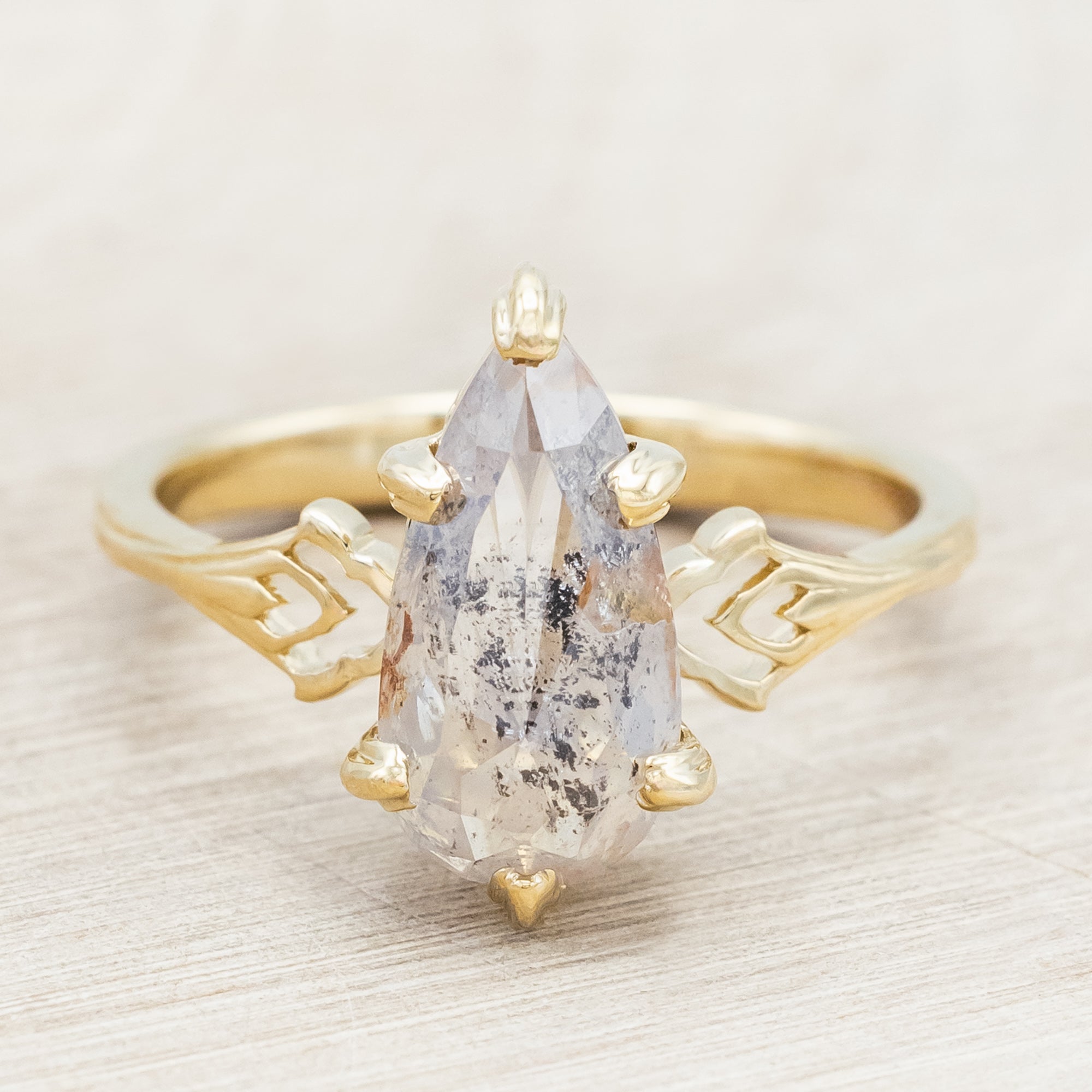 Gold ring with a pear cut salt & pepper diamond on a light wooden surface