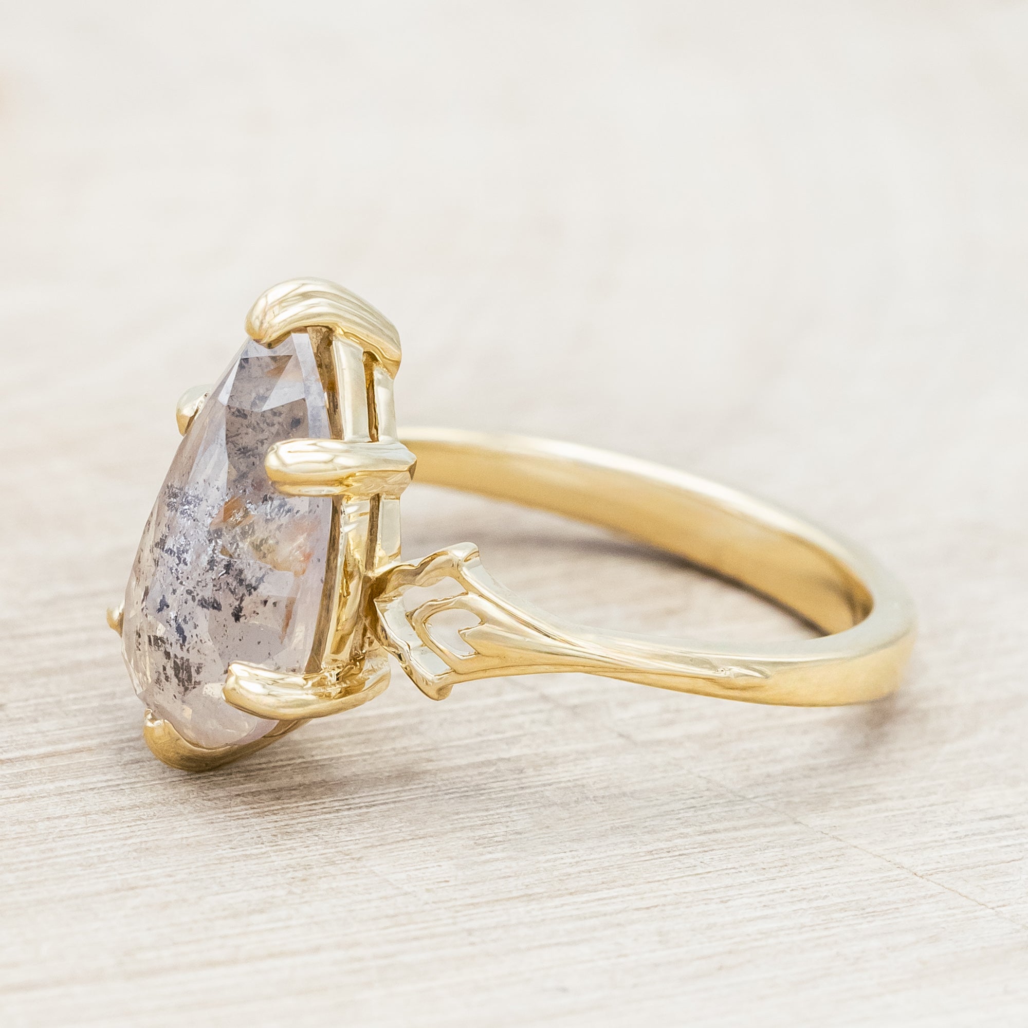 Gold ring with a pear cut salt & pepper diamond on a light wooden surface