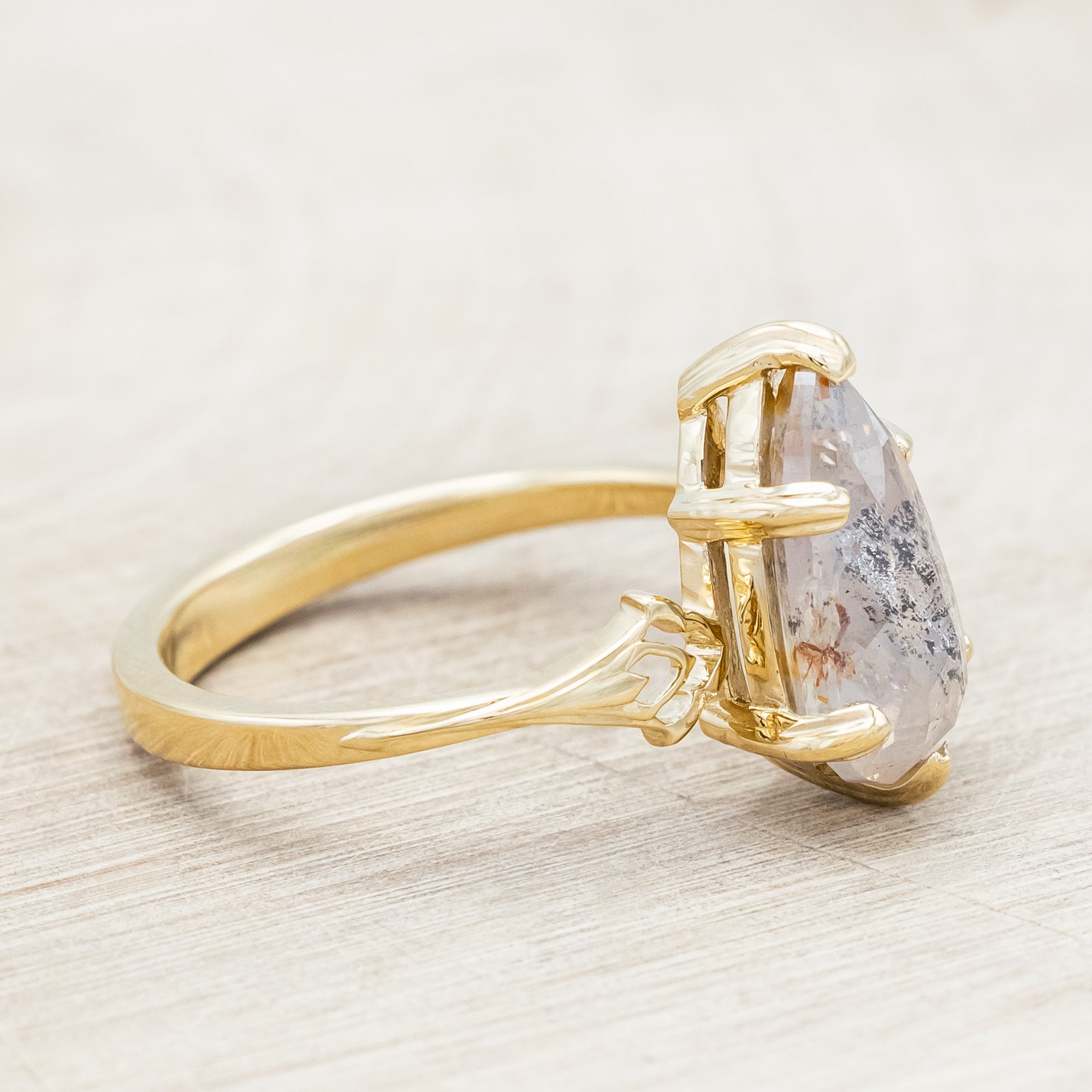 Gold ring with a pear cut salt & pepper diamond on a light wooden surface