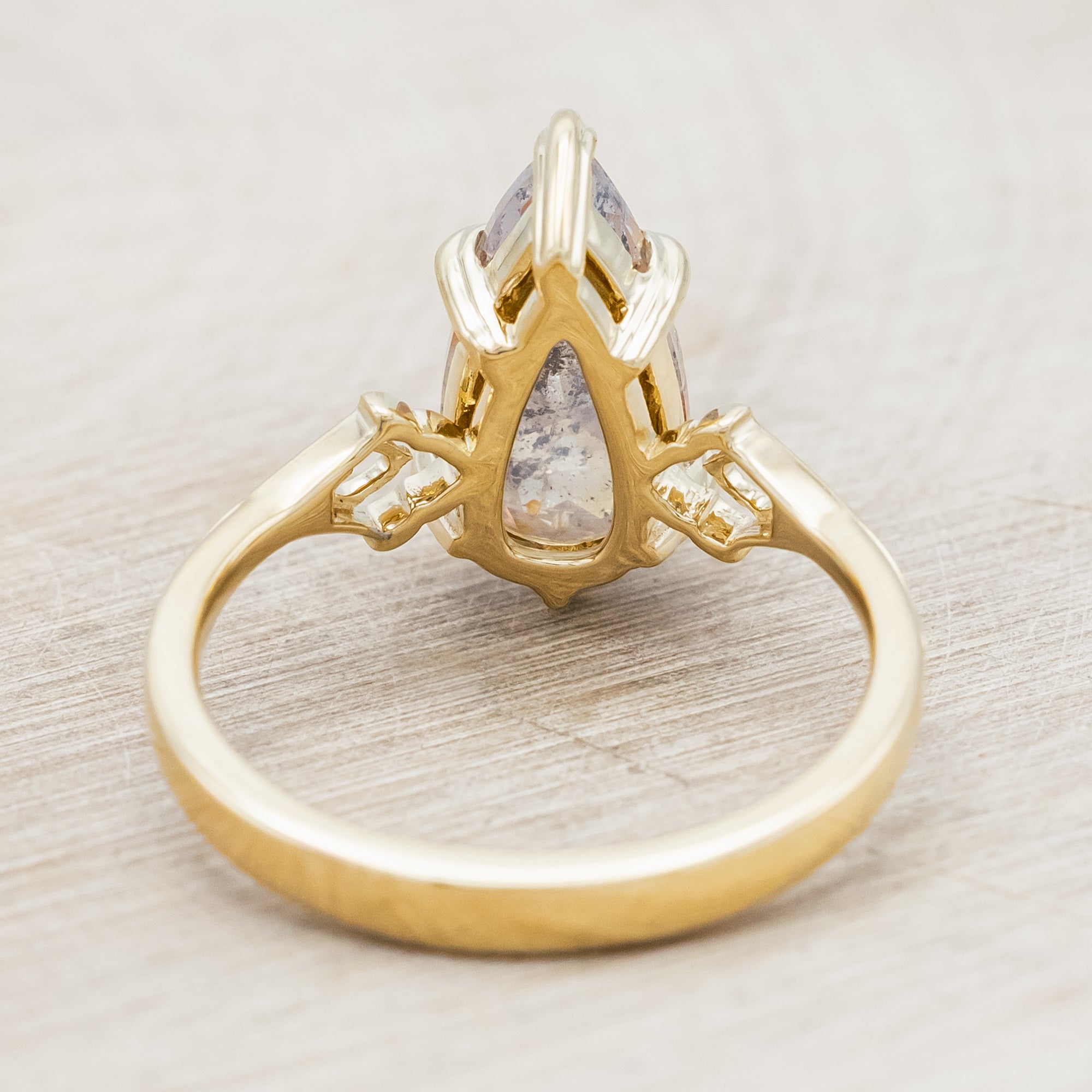 Gold ring with a pear cut salt & pepper diamond on a light wooden surface