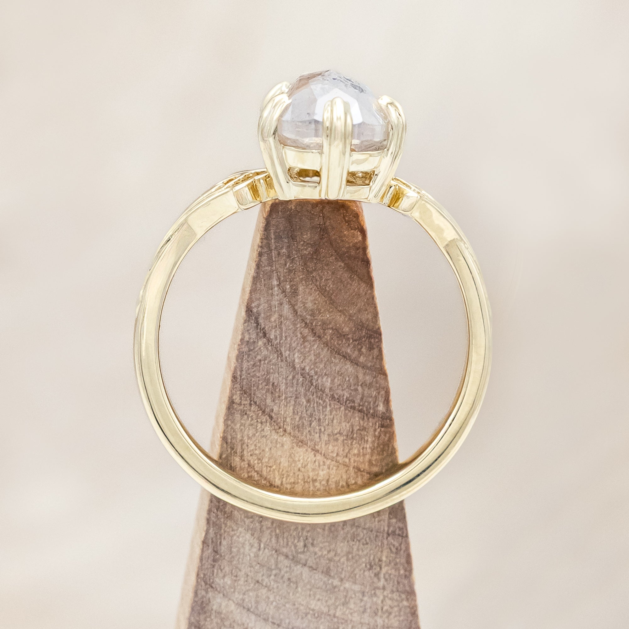 Gold ring with a pear cut salt & pepper diamond on a light wooden surface
