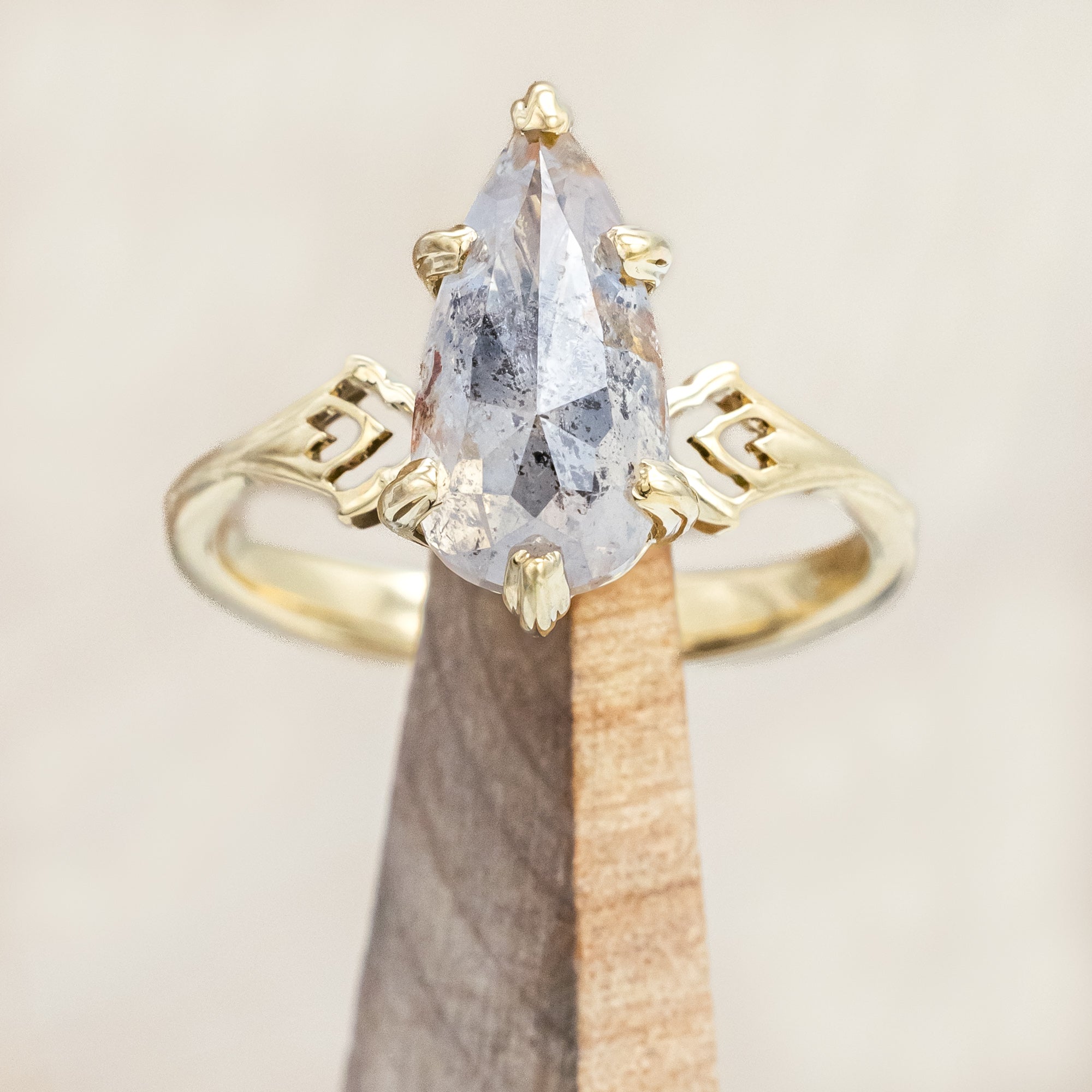 Gold ring with a pear cut salt & pepper diamond on a wooden stand against a beige background