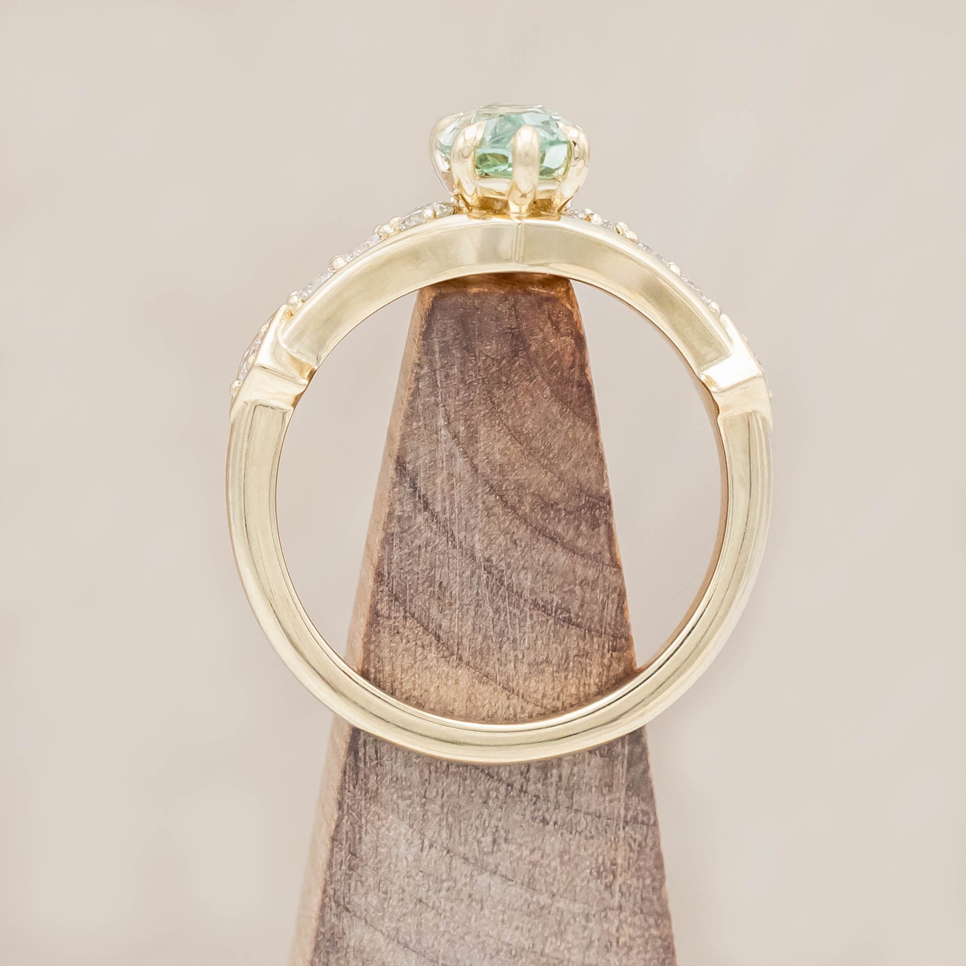 Gold ring with a green sapphire and diamonds on a beige background