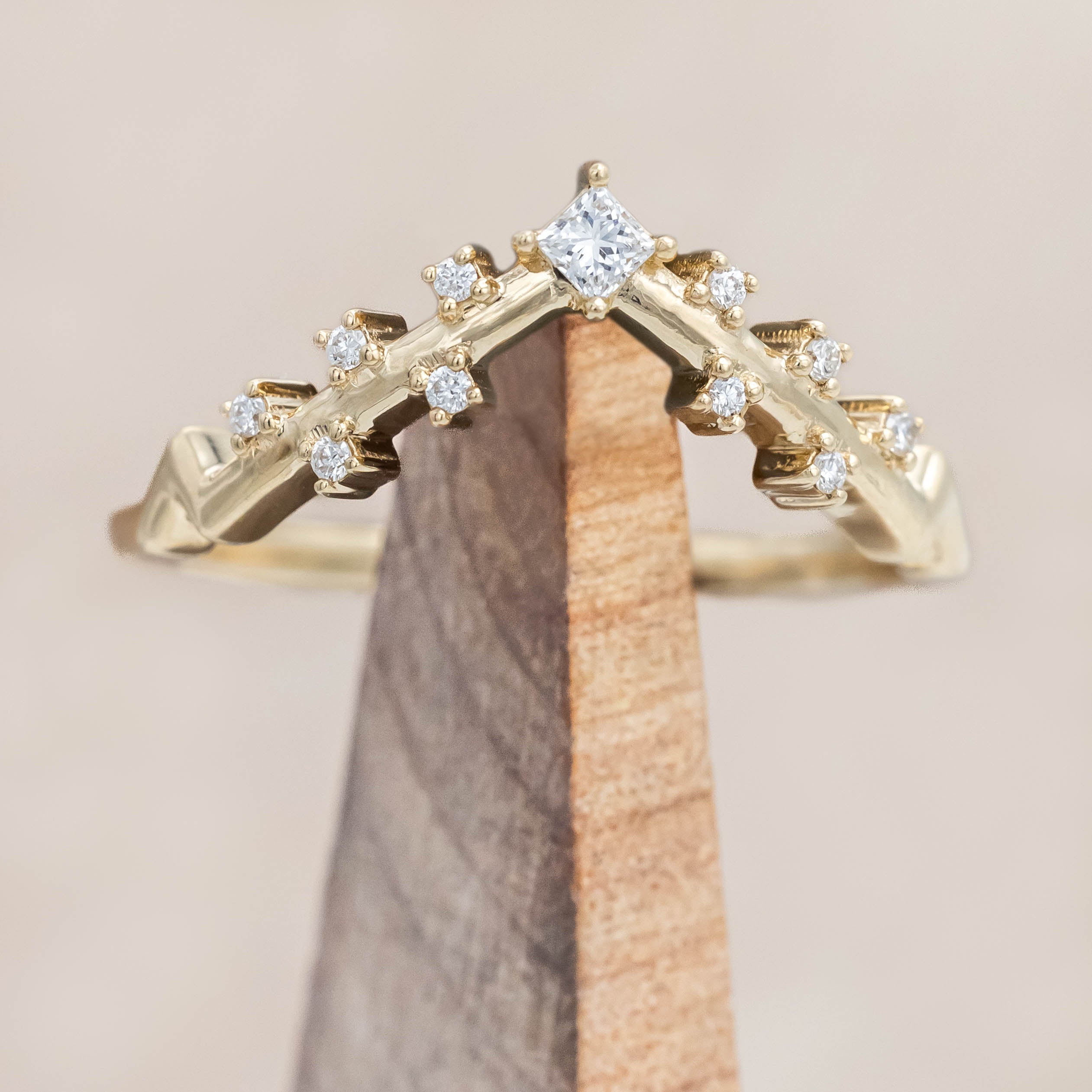Gold ring with diamonds on a wooden stand against a beige background