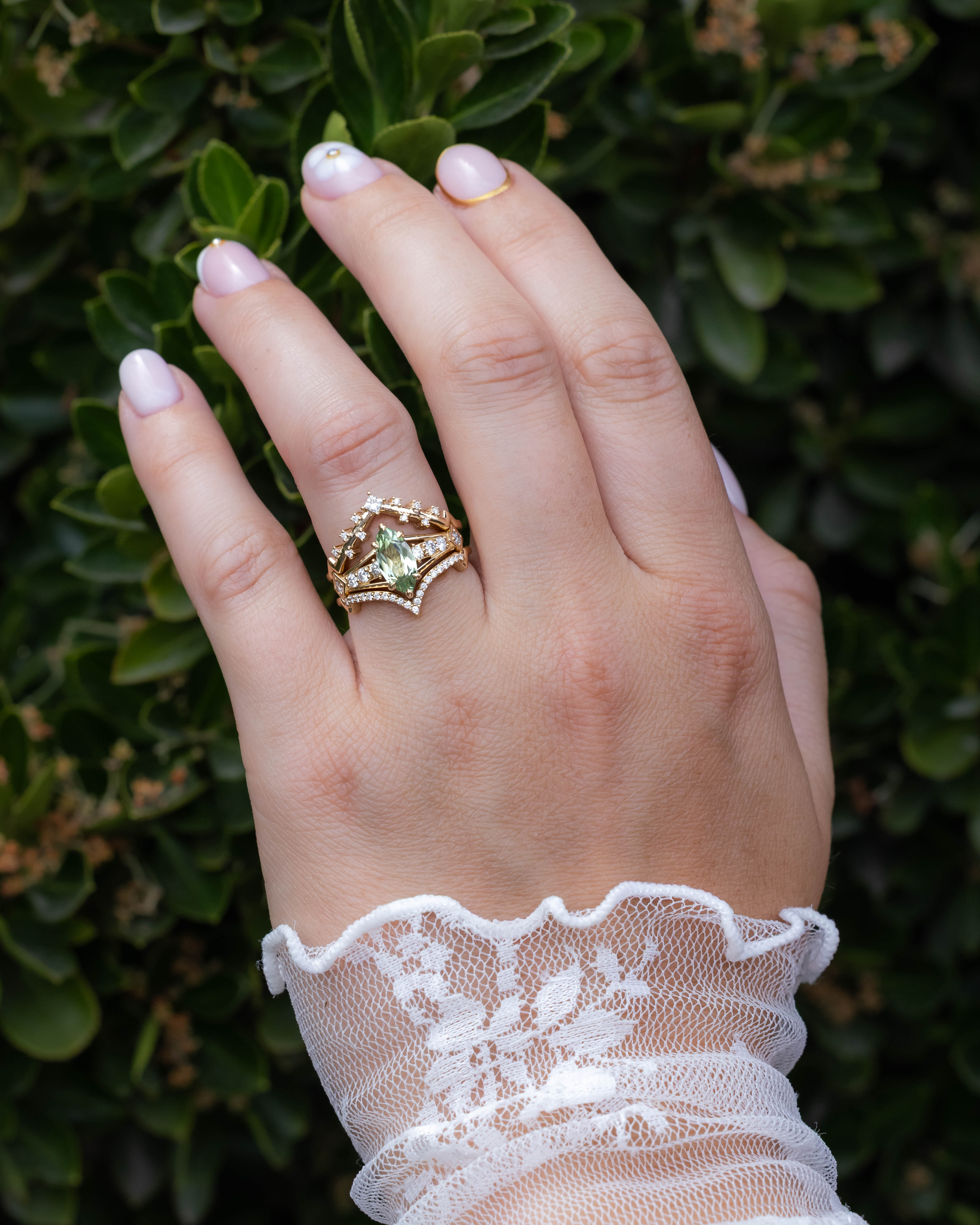 Hand wearing a gold ring with a green sapphire against a green leafy background