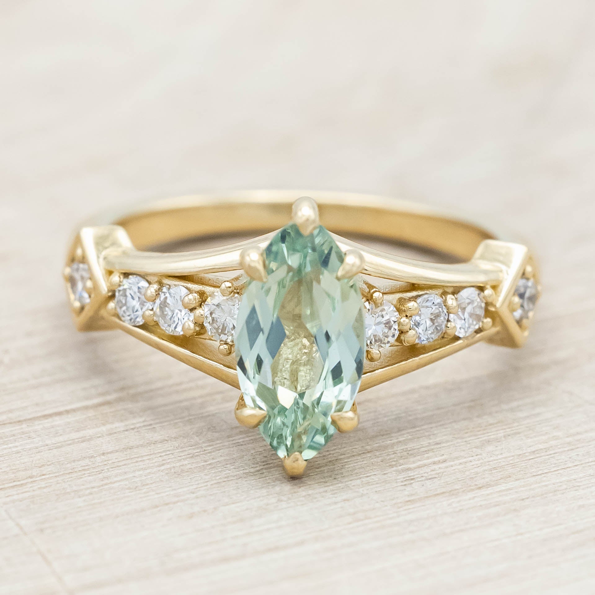 Gold ring with a green sapphire and diamonds on a beige background