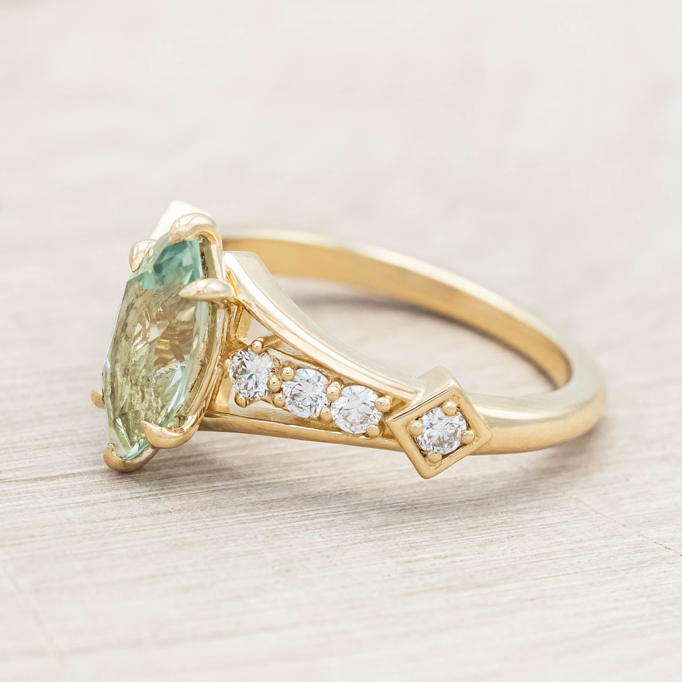 Gold ring with a green sapphire and diamonds on a beige background