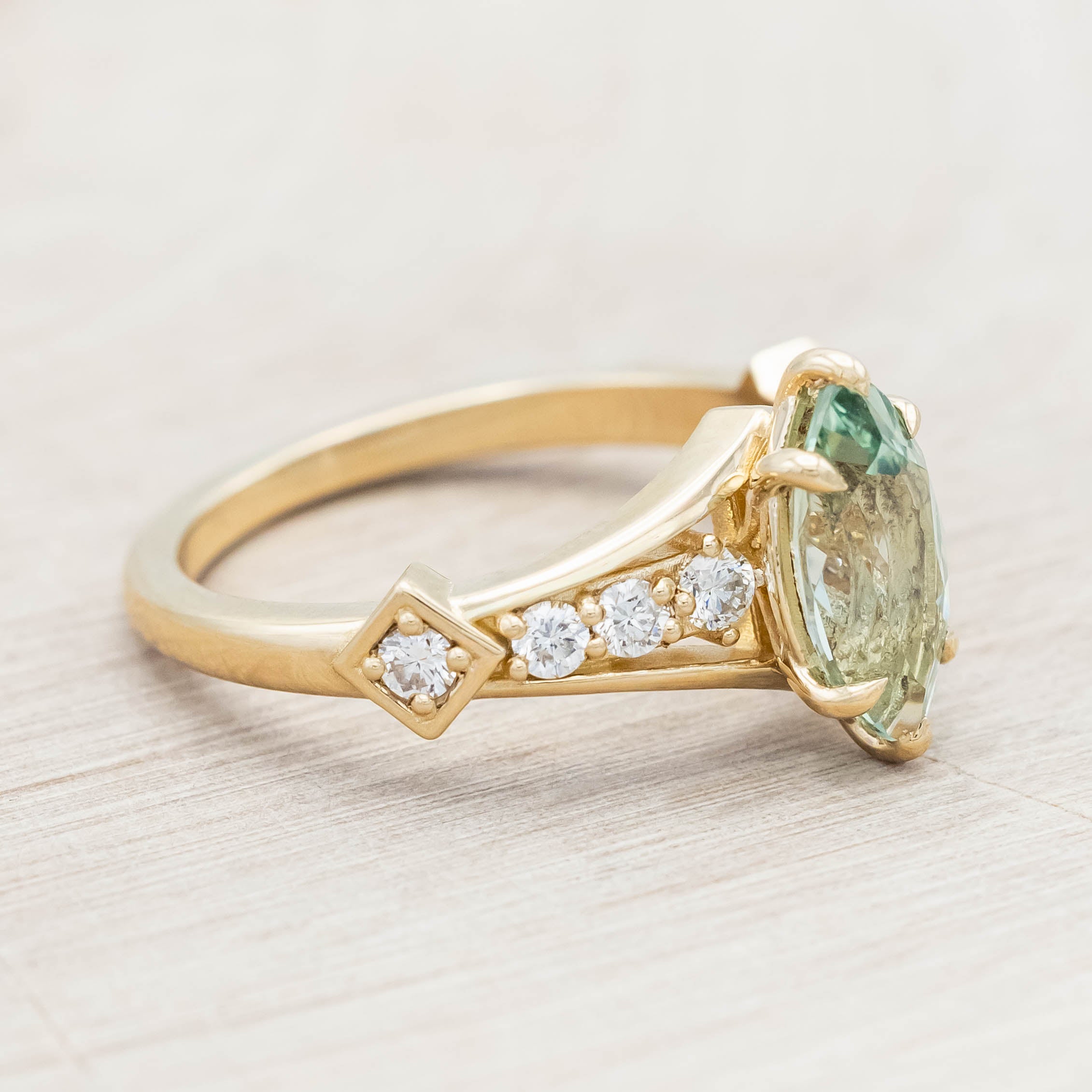 Gold ring with a green sapphire and diamonds on a beige background