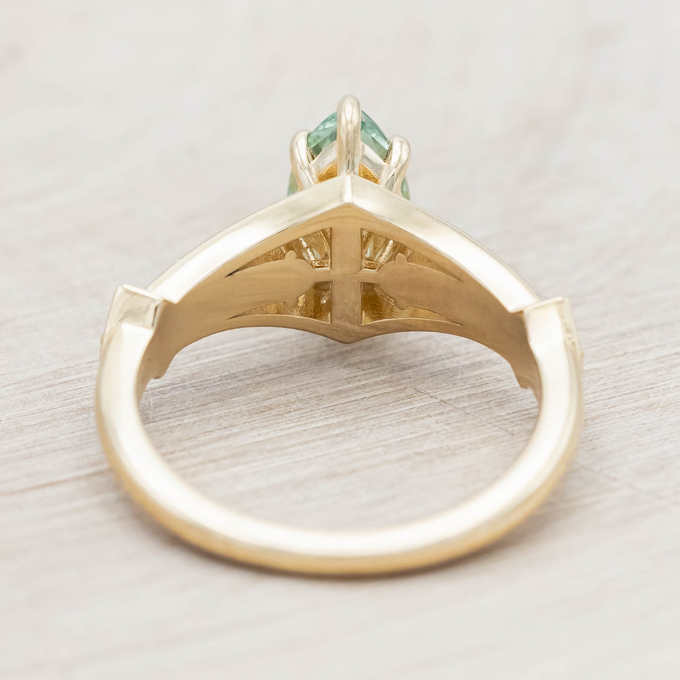 Gold ring with a green sapphire and diamonds on a beige background