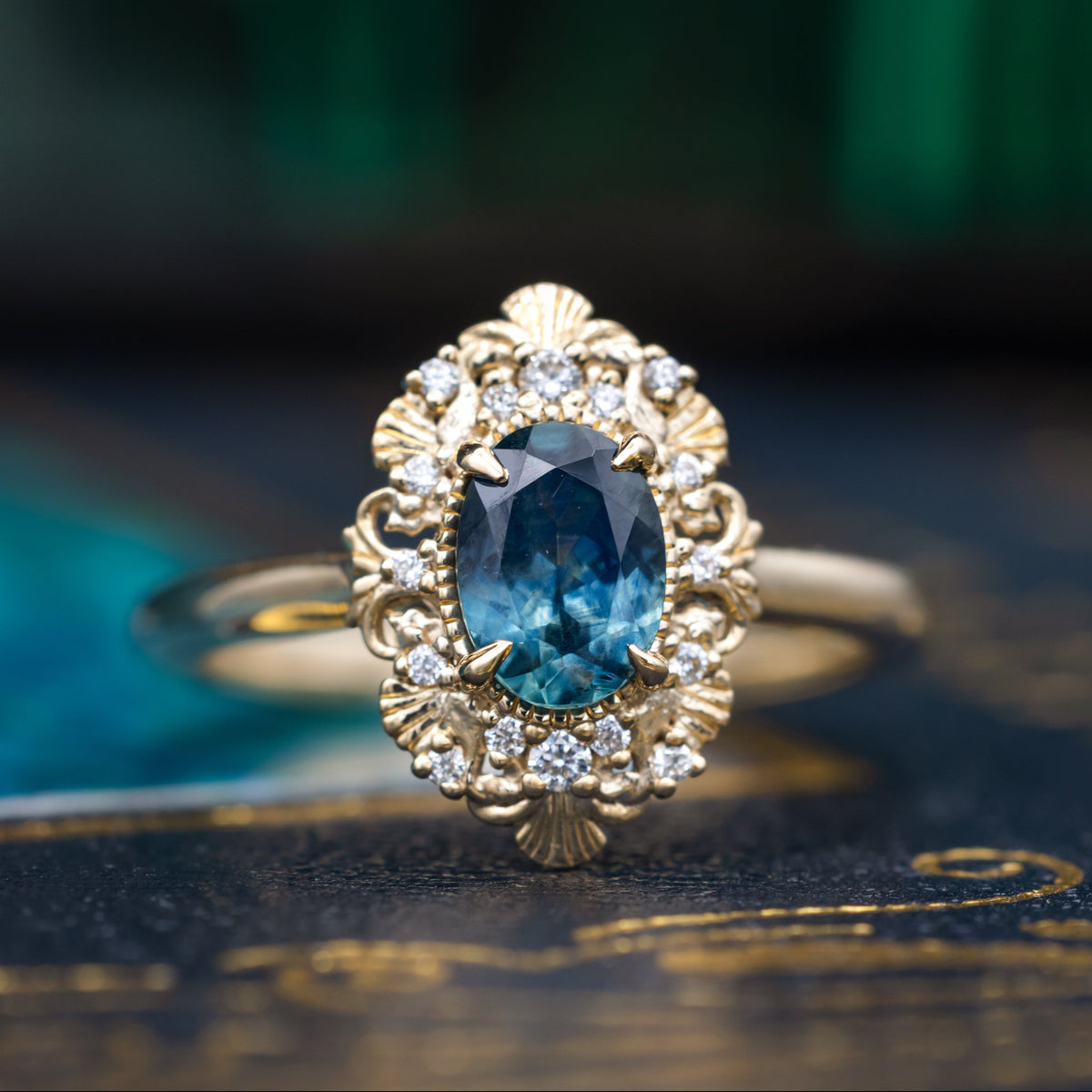 A gold ring with Montana sapphire center stone and diamond accents against a dark moody background