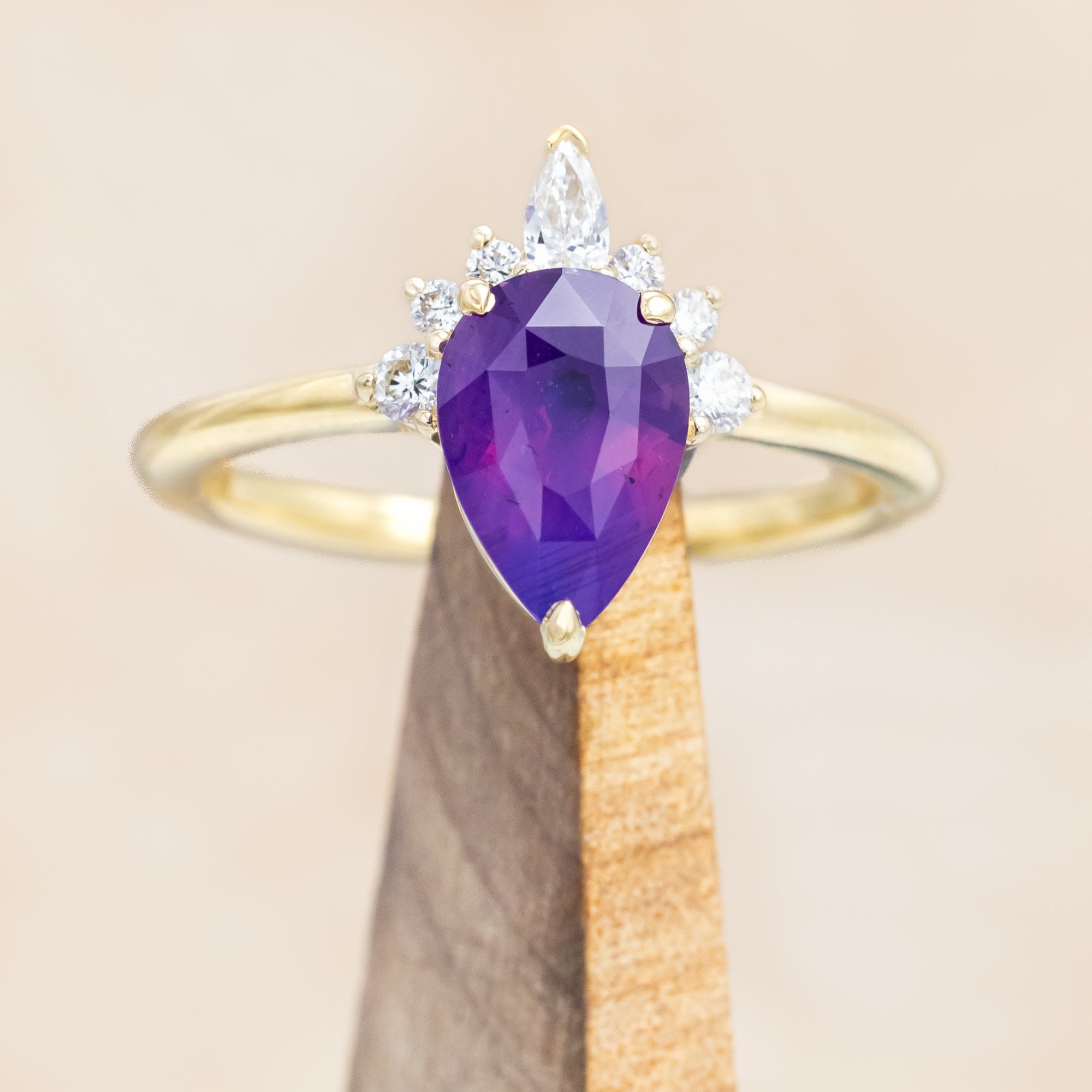 14K gold ring with a pear Sri Lankan sapphire on a wooden stand against a beige background