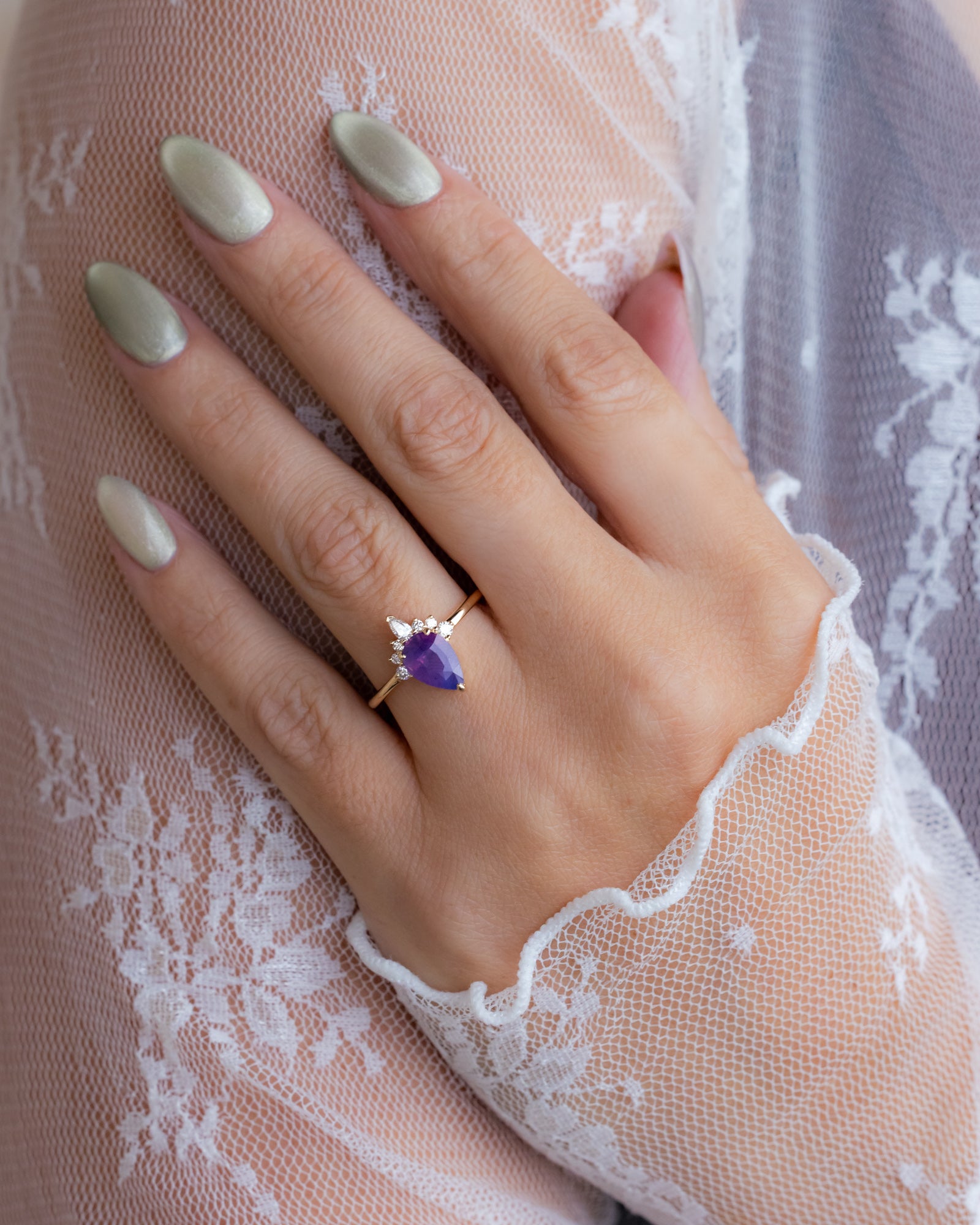 Hand wearing a ring with a Sri Lankan sapphire on a lace fabric background