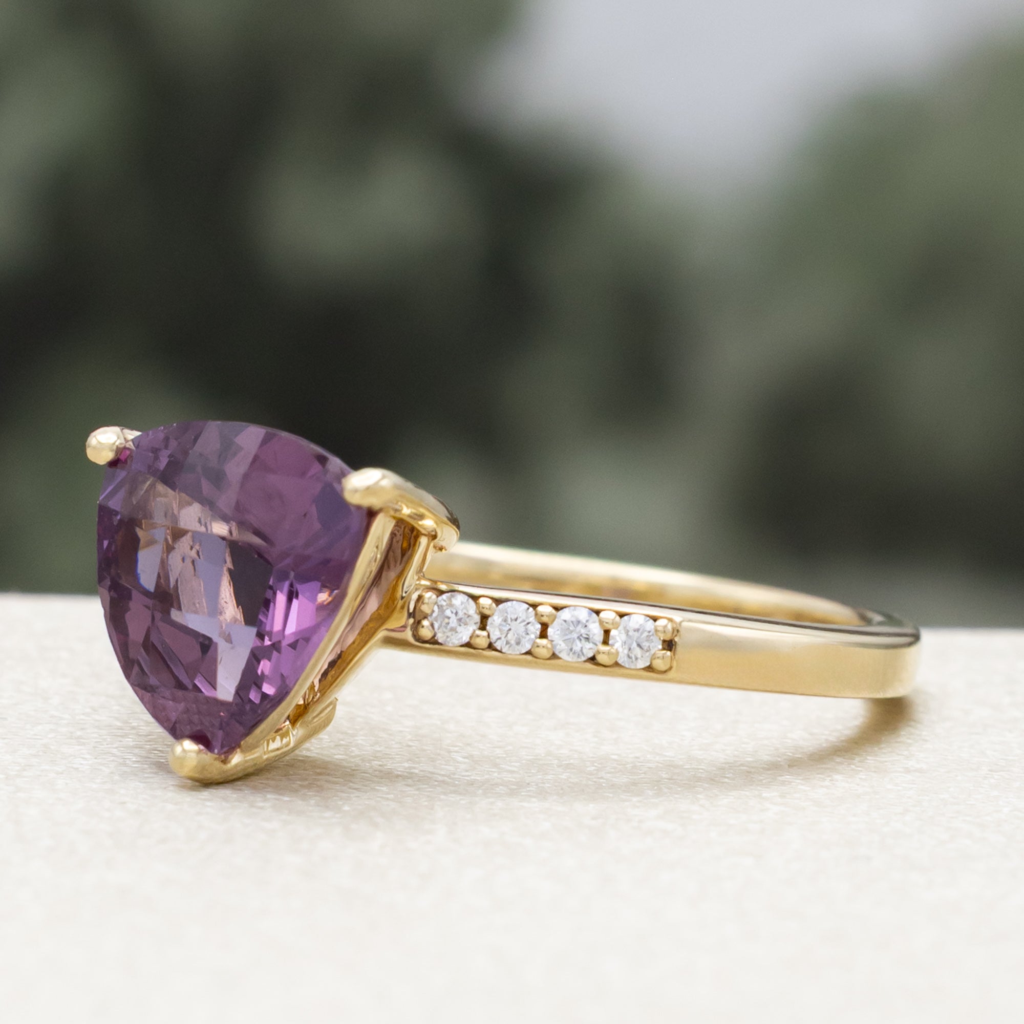 Gold ring with a purple garnet and diamond accents on a blurred background