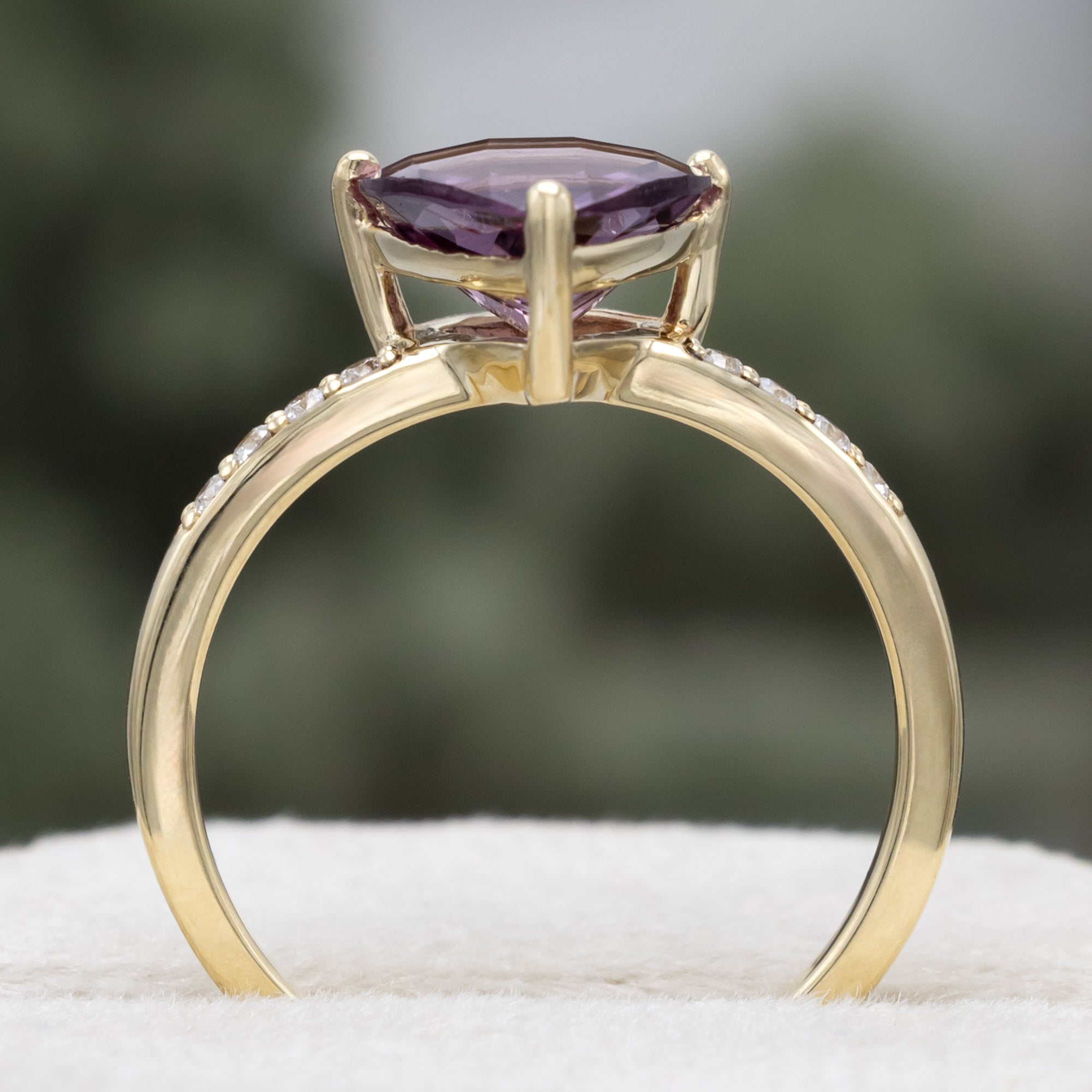 Gold ring with a purple garnet and diamond accents on a blurred background