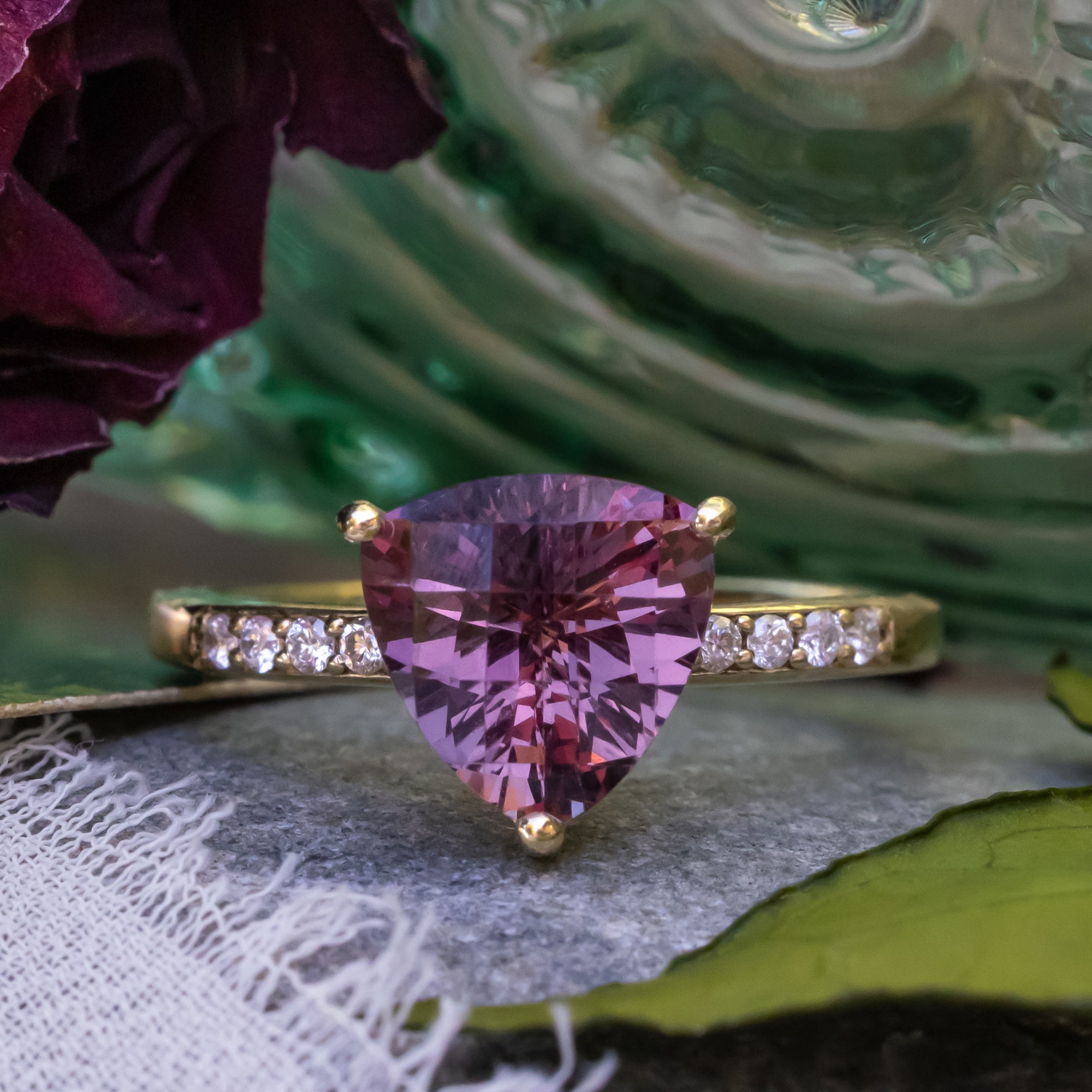 Gold ring with purple garnet and diamond accents on a textured surface.