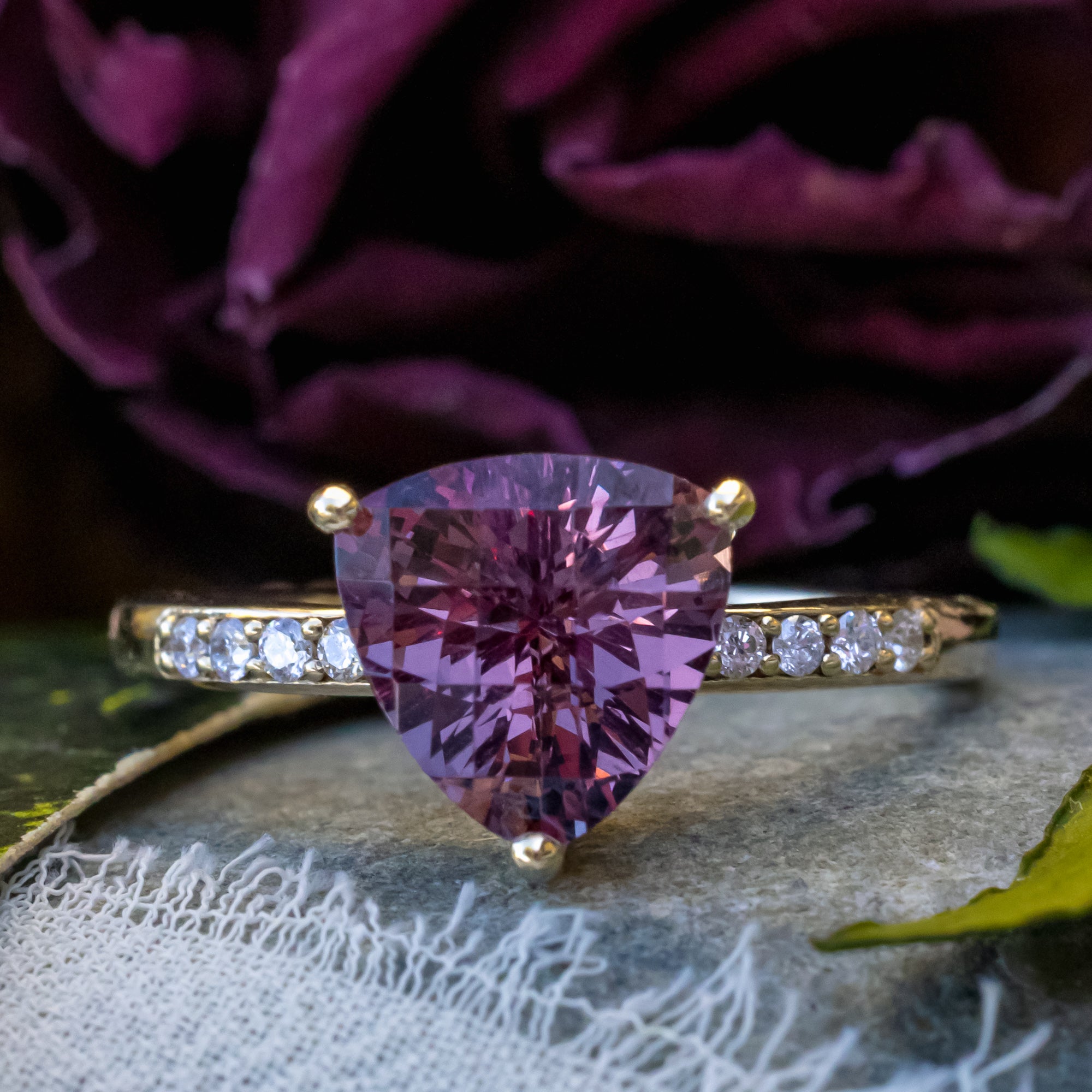 Gold ring with purple garnet and diamond accents on a textured surface.