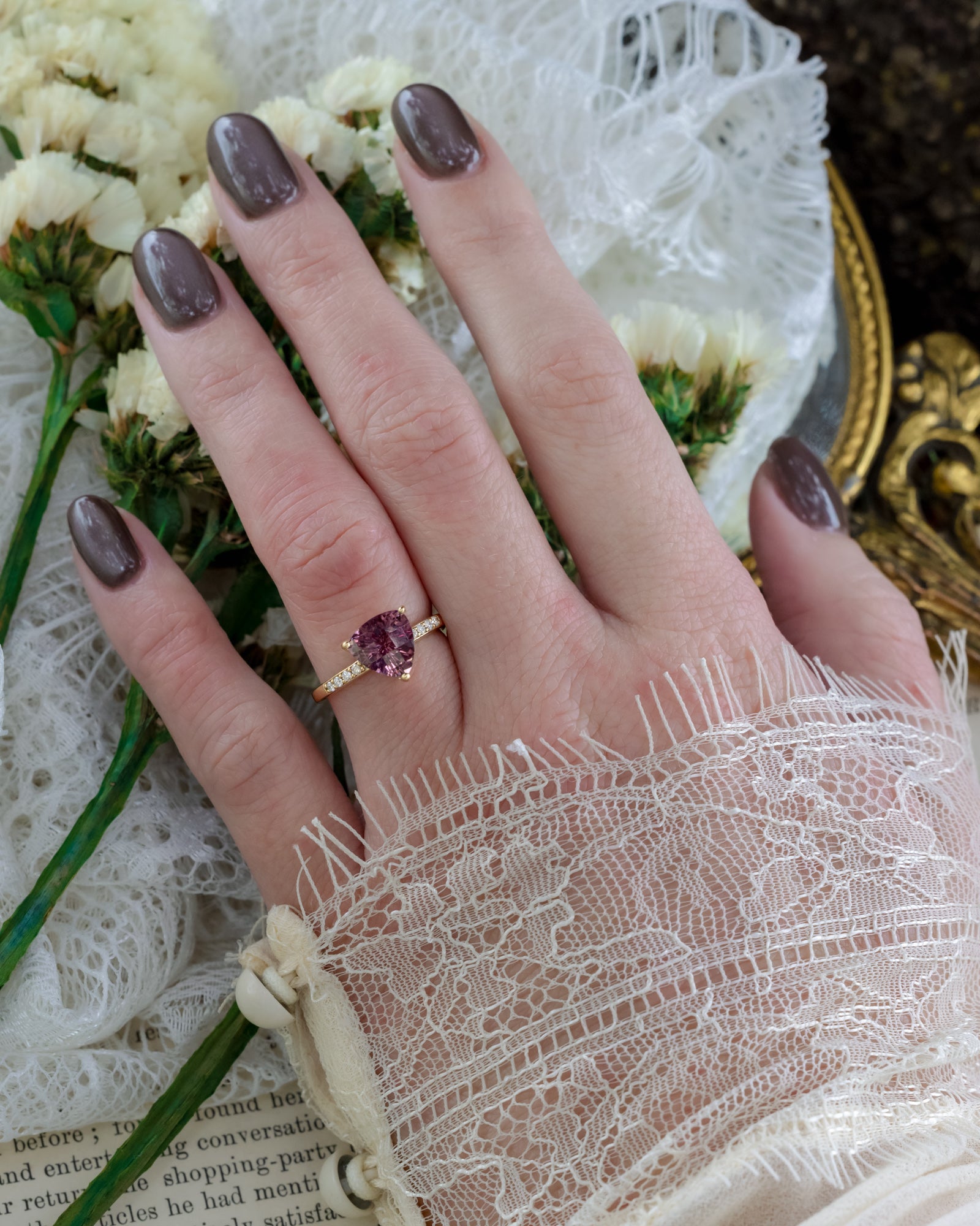 Hand wearing a gold ring with a purple garnet against a floral background