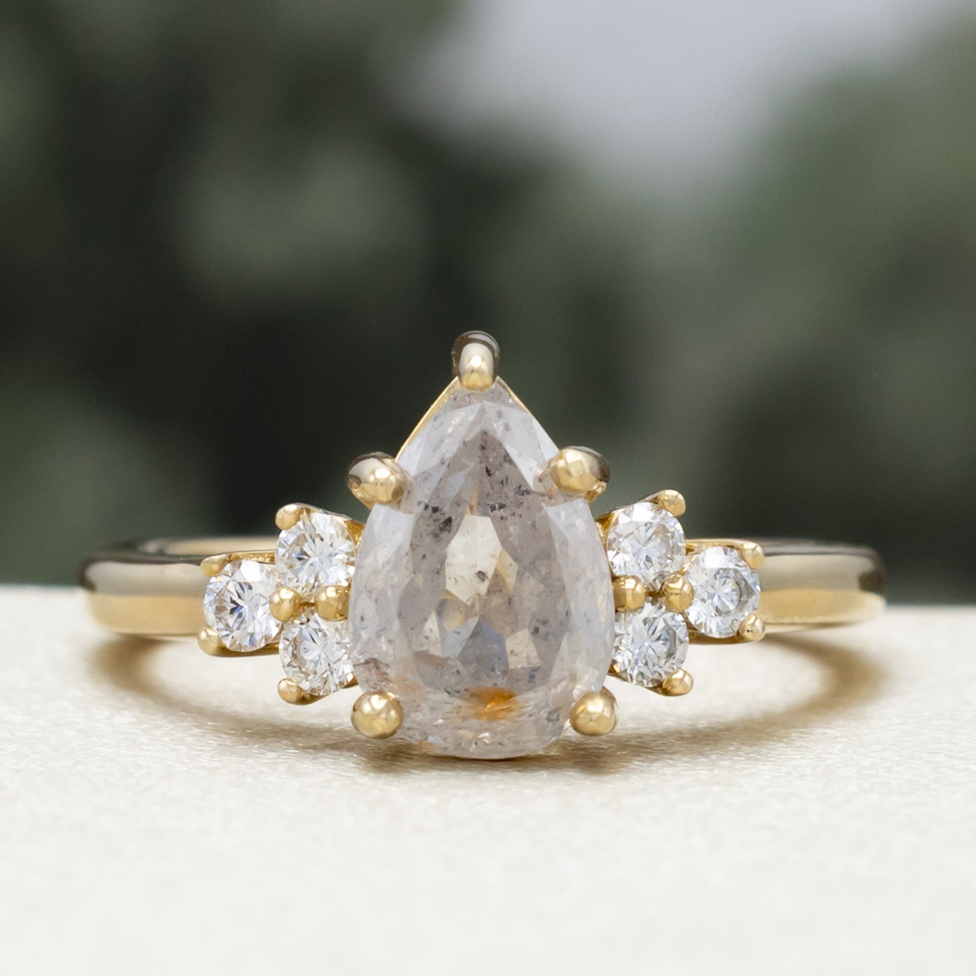 Gold ring with pear cut salt & pepper diamond and diamond accents against a blurred green background