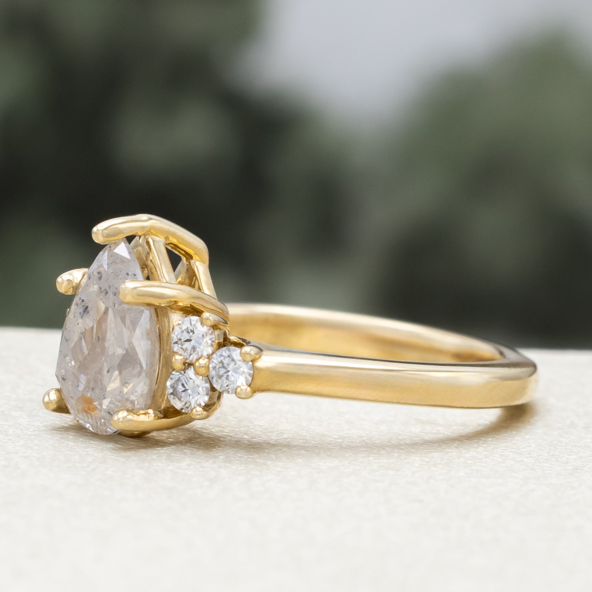 Gold ring with pear cut salt & pepper diamond and diamond accents against a blurred green background