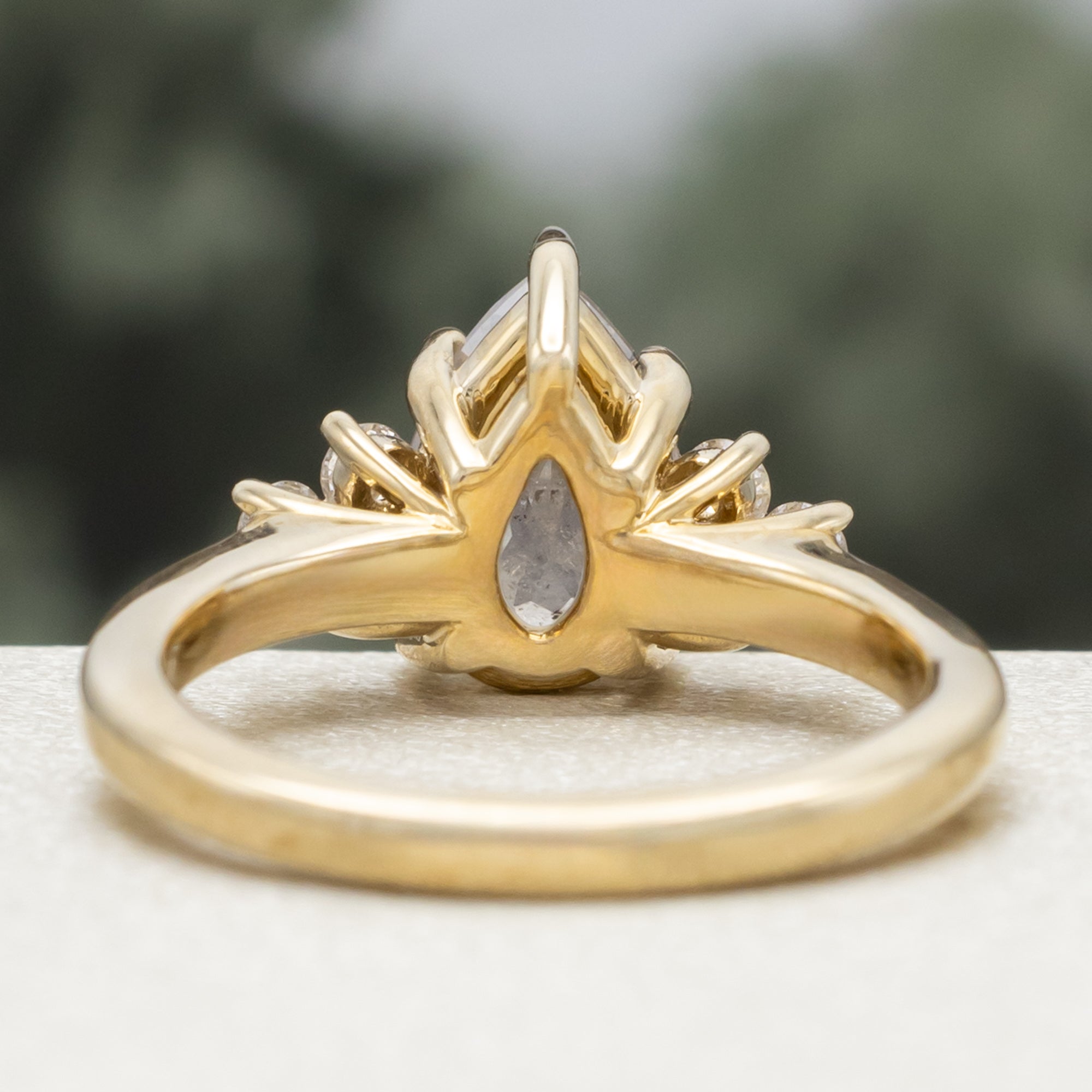 Gold ring with pear cut salt & pepper diamond and diamond accents against a blurred green background
