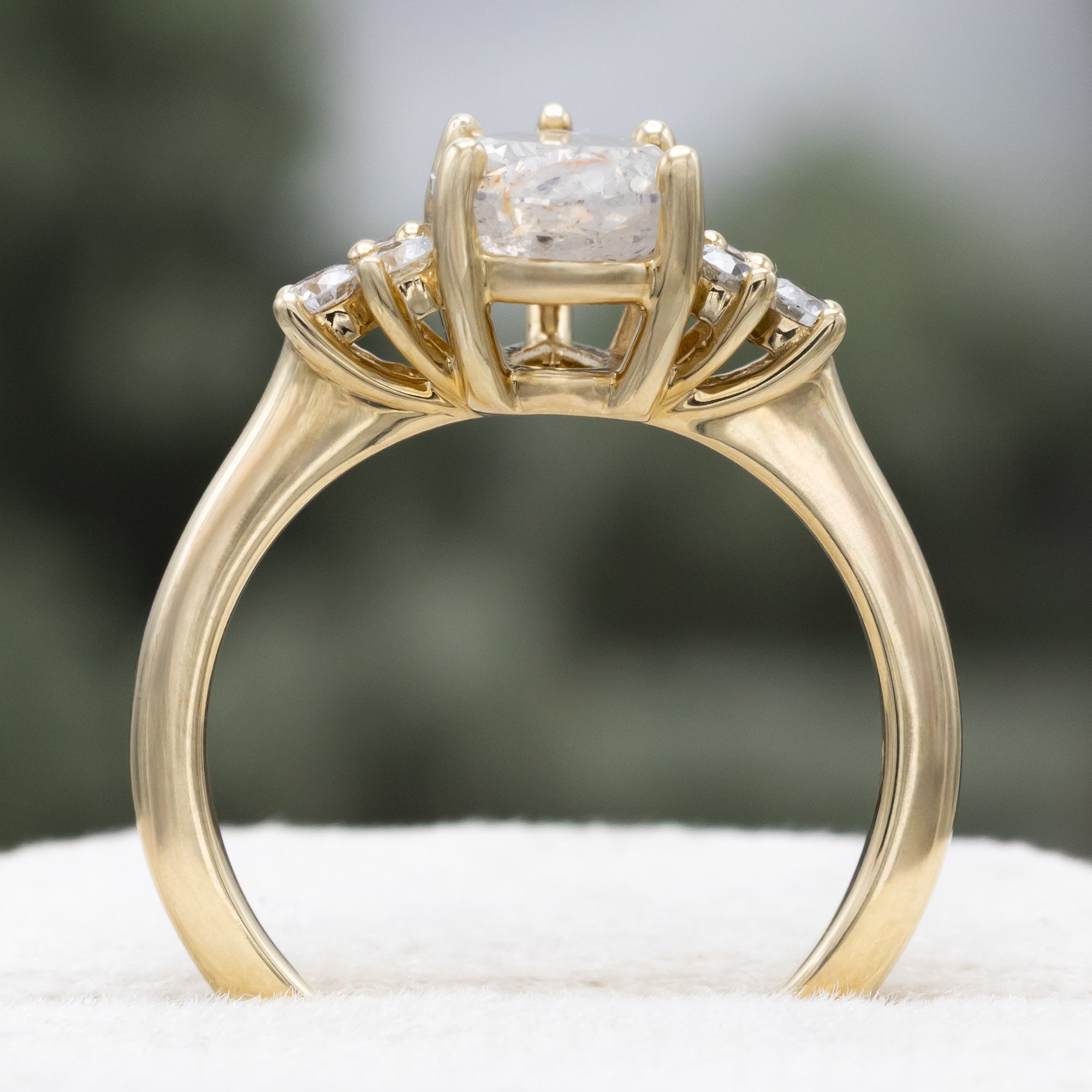 Gold ring with pear cut salt & pepper diamond and diamond accents against a blurred green background
