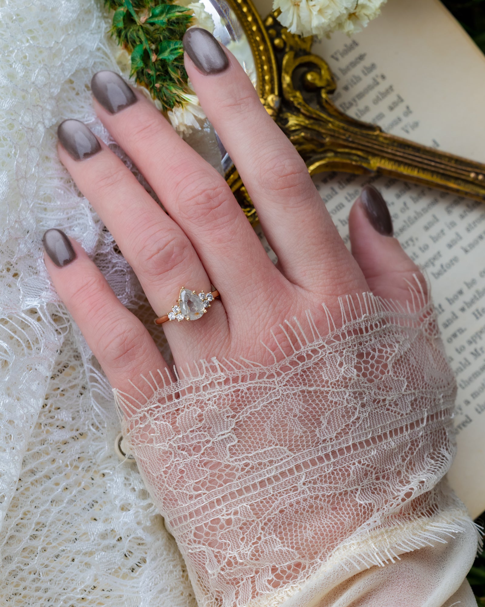 Hand wearing gold ring pear cut salt & pepper diamond against a lace background