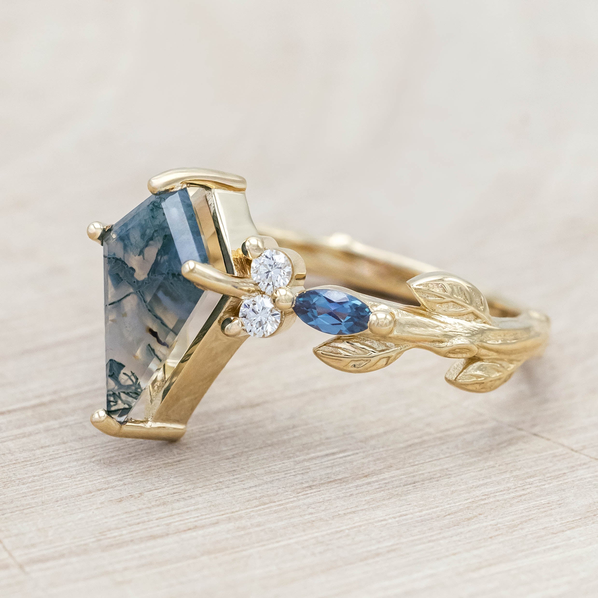 Gold ring with moss agate center stone with alexandrite & diamond accents on a light wooden surface