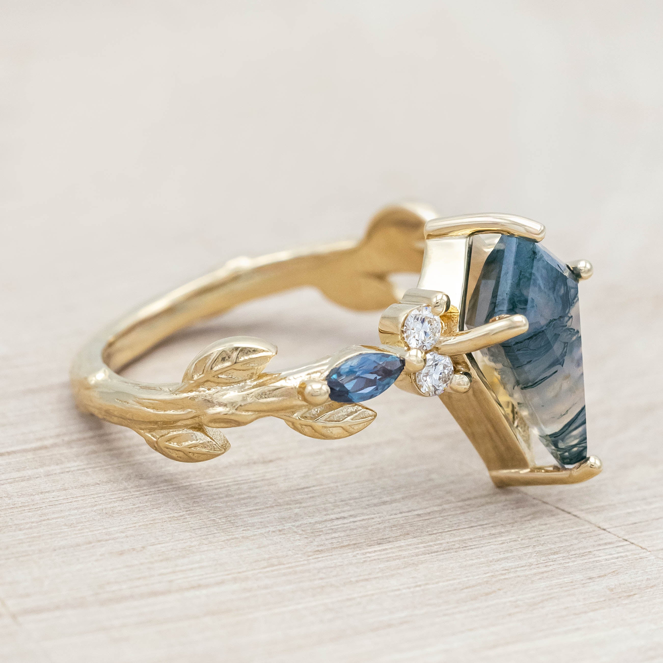 Gold ring with moss agate center stone with alexandrite & diamond accents on a light wooden surface
